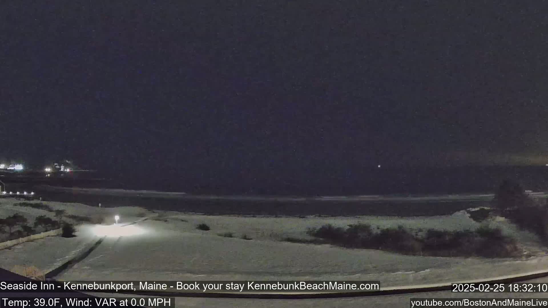 A nighttime view of a snow-covered beach and road with a dark, clear sky and calm ocean.