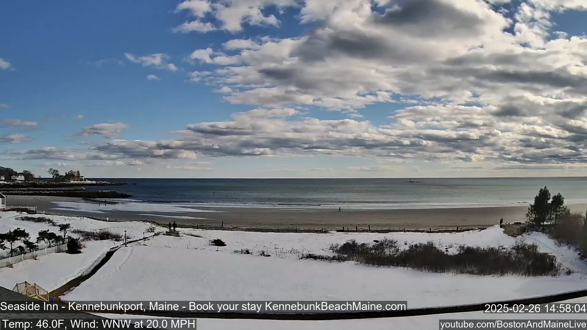 A partly cloudy, windy day at a snow-covered beach with a calm ocean in the background.
