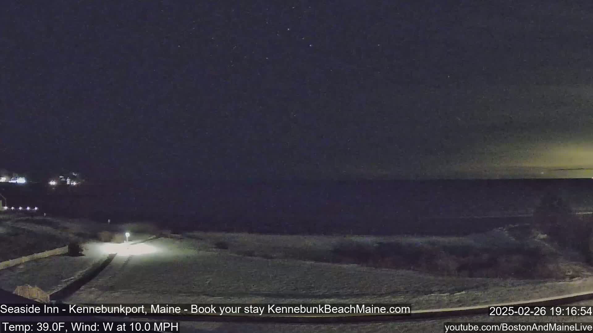 A nighttime view of a snow-covered landscape overlooking a dark ocean under a clear, starry sky.
