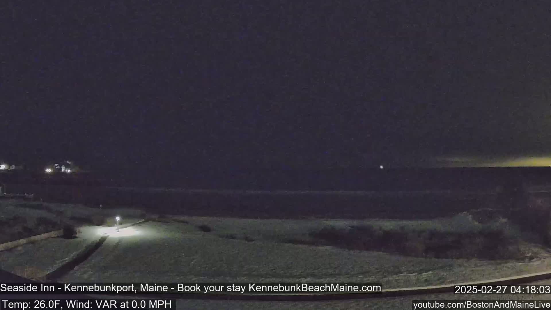 A snow-covered landscape at night shows a dark ocean in the distance under a mostly clear sky.
