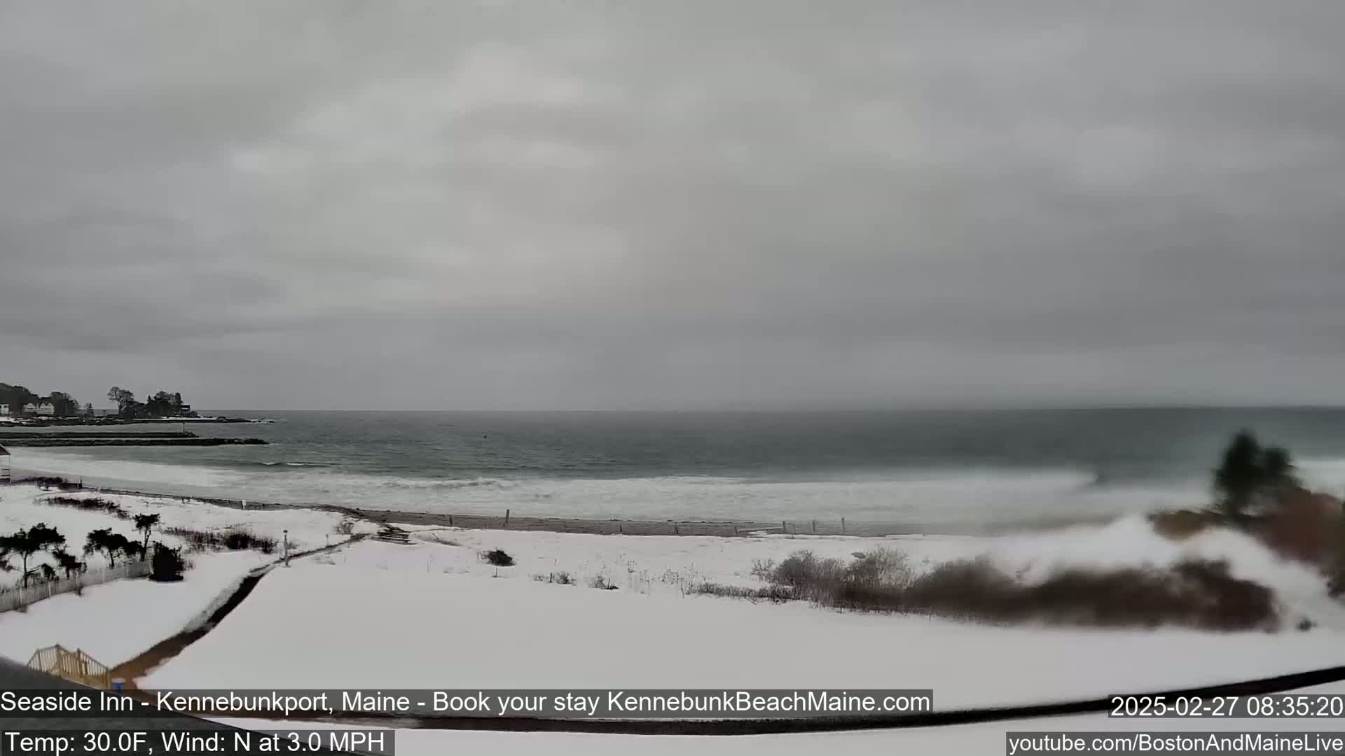 A snow-covered beach with a gray, overcast sky and a choppy ocean is visible from a high vantage point.