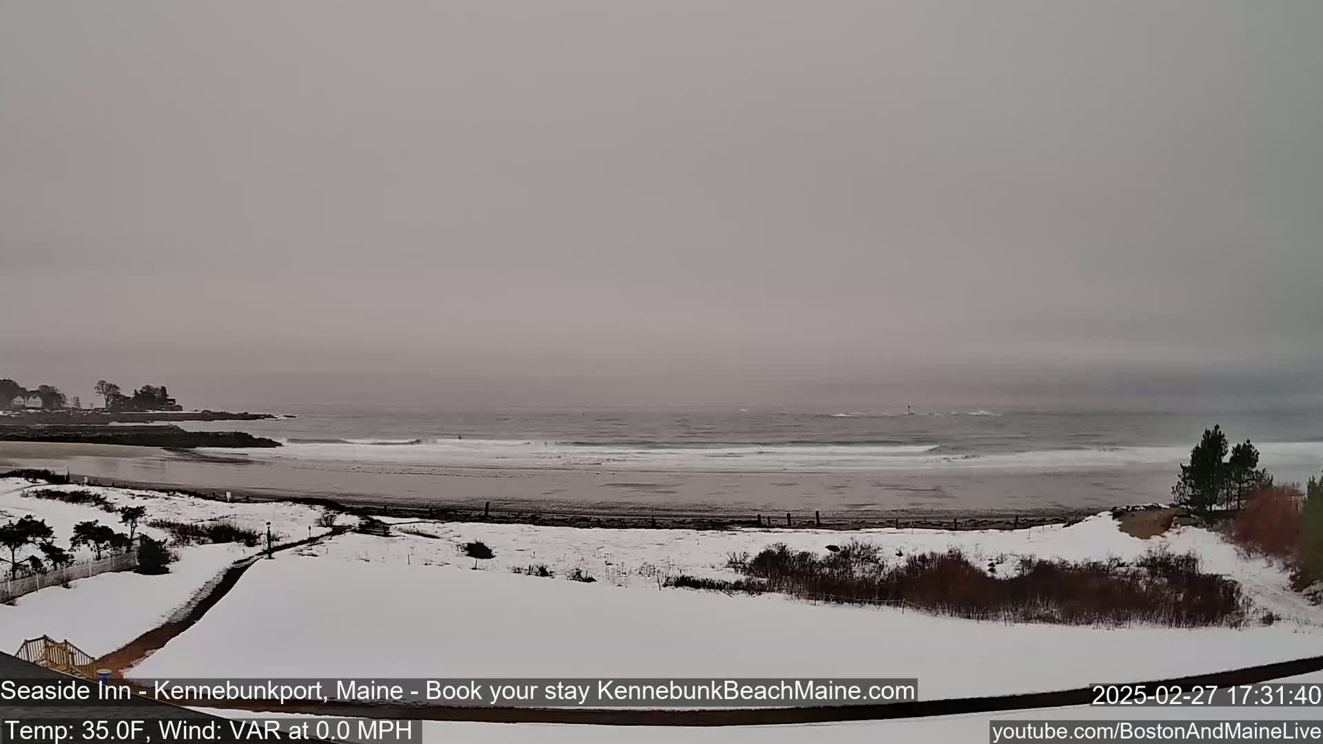 A snow-covered beach and shoreline are visible under an overcast sky, with gentle waves rolling onto the shore.