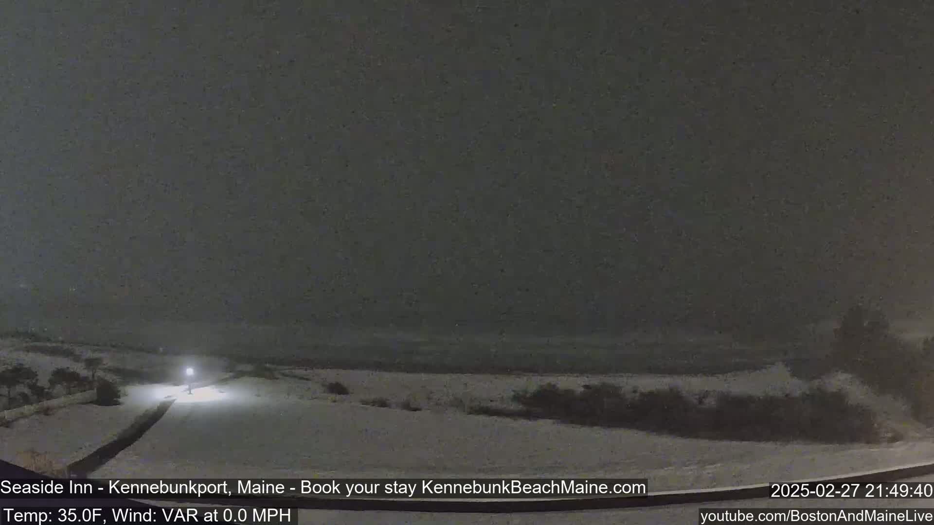 A snow-covered landscape is illuminated by a single light at night under a dark, snowy sky.