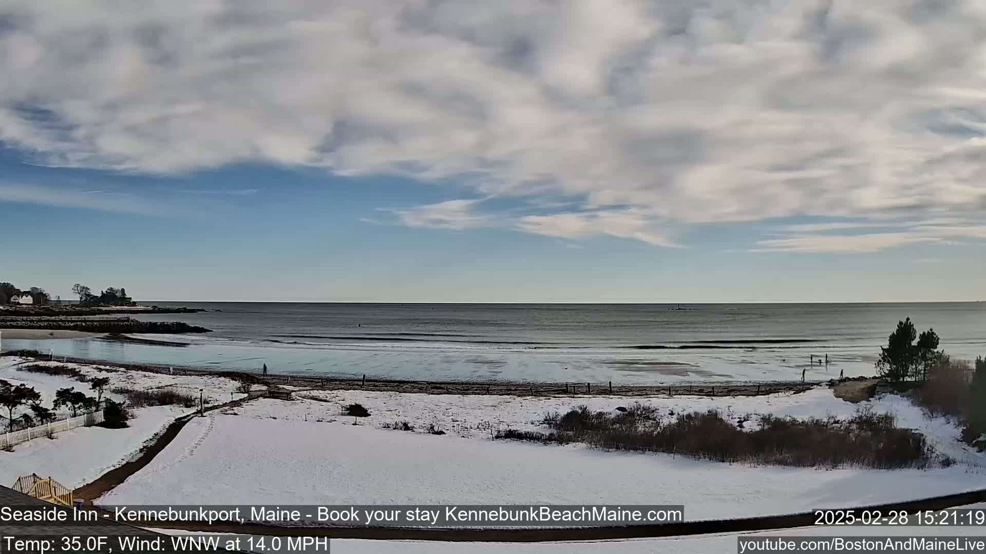 A partly cloudy sky overlooks a snow-covered beach with a calm ocean, under a 35°F temperature with a 14 mph wind from the west-northwest.