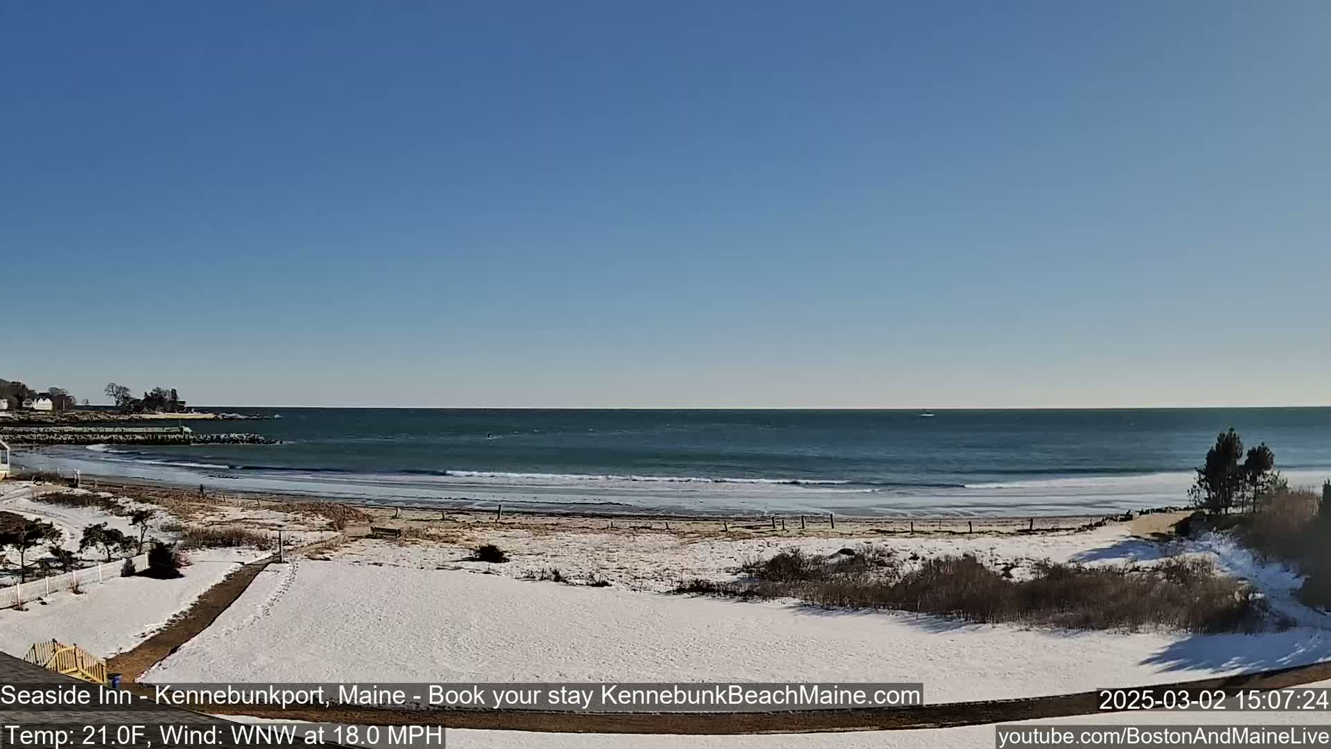 A snow-covered beach with a calm ocean under a clear blue sky.