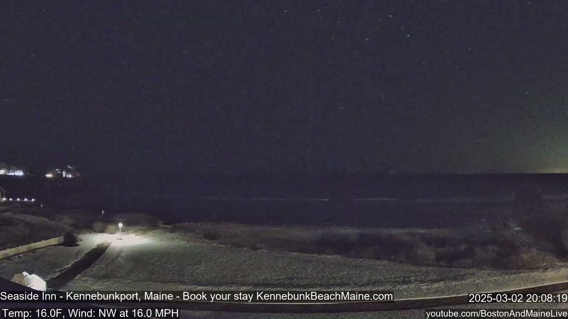 A nighttime view of a snow-covered landscape leading to a dark ocean under a starry sky.