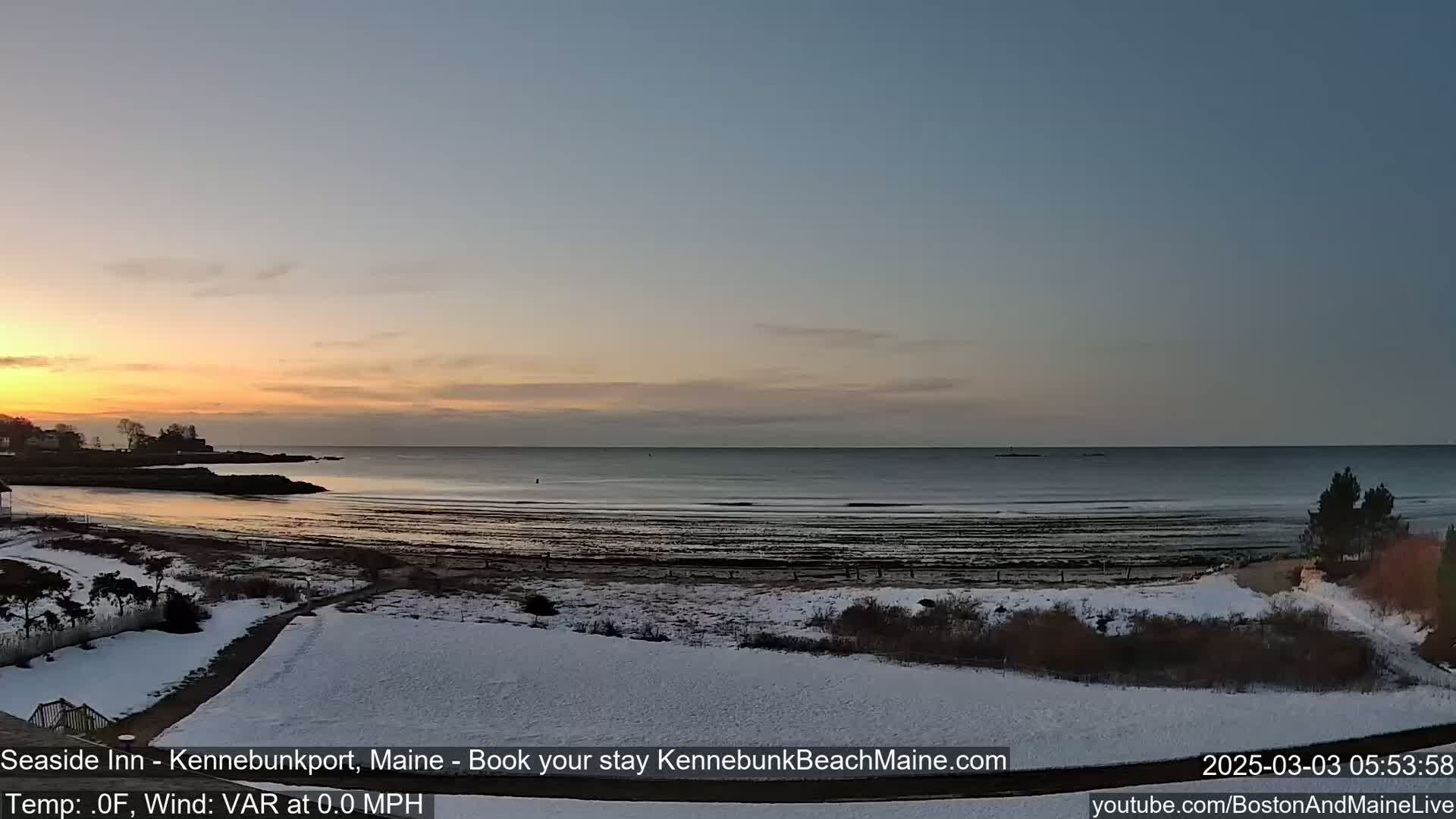 A snow-covered beach at sunrise overlooks a calm ocean.