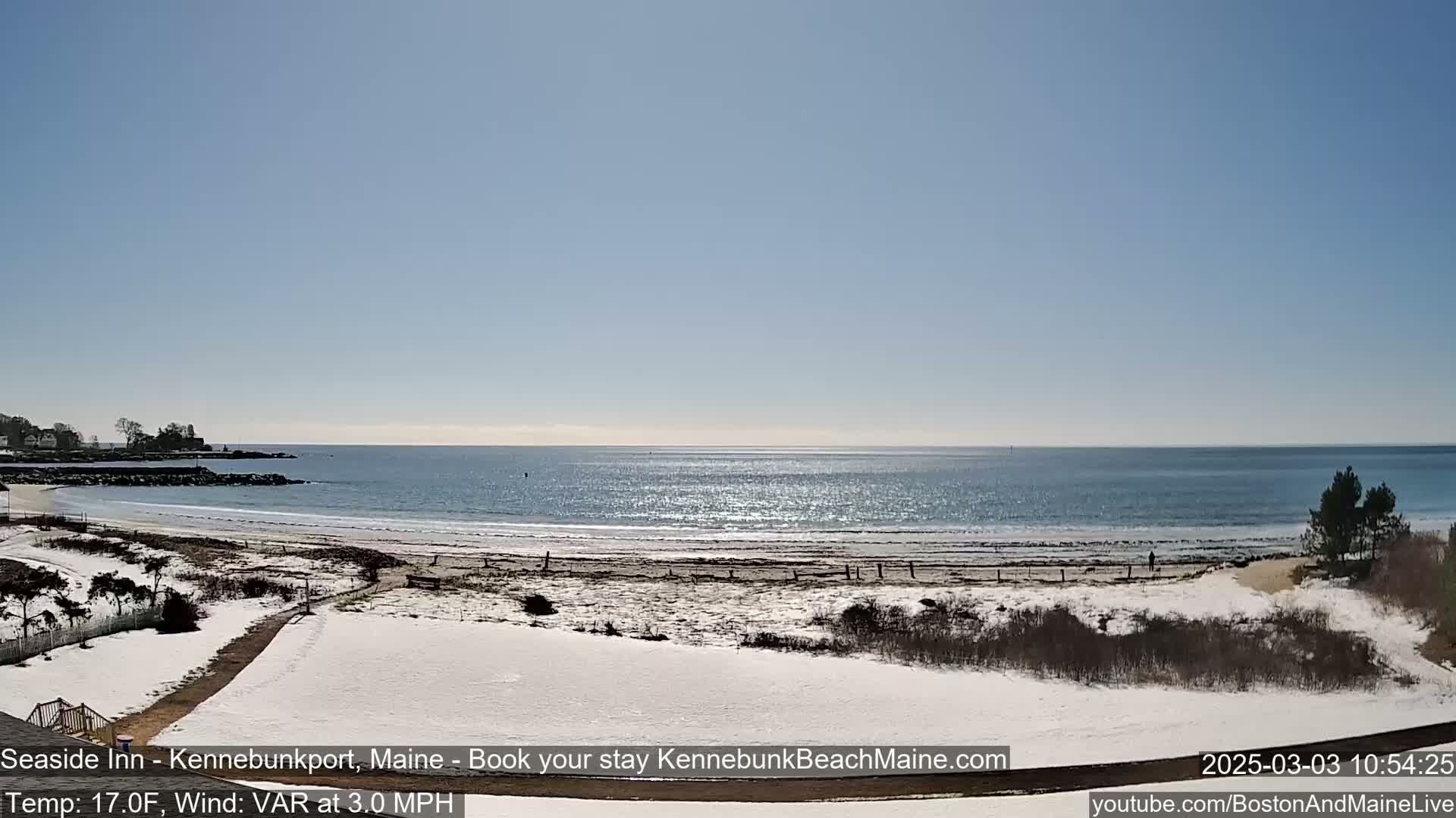 A snow-covered beach with a calm ocean under a clear blue sky.