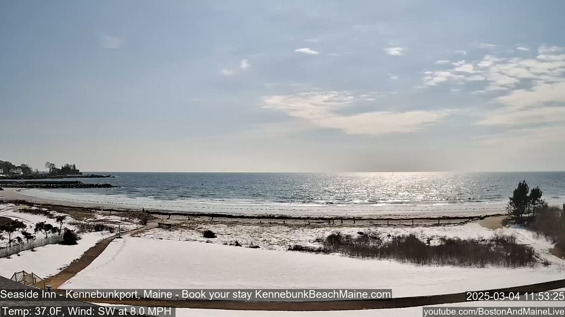 A partly sunny, snowy beach scene with a calm ocean under a mostly clear sky.