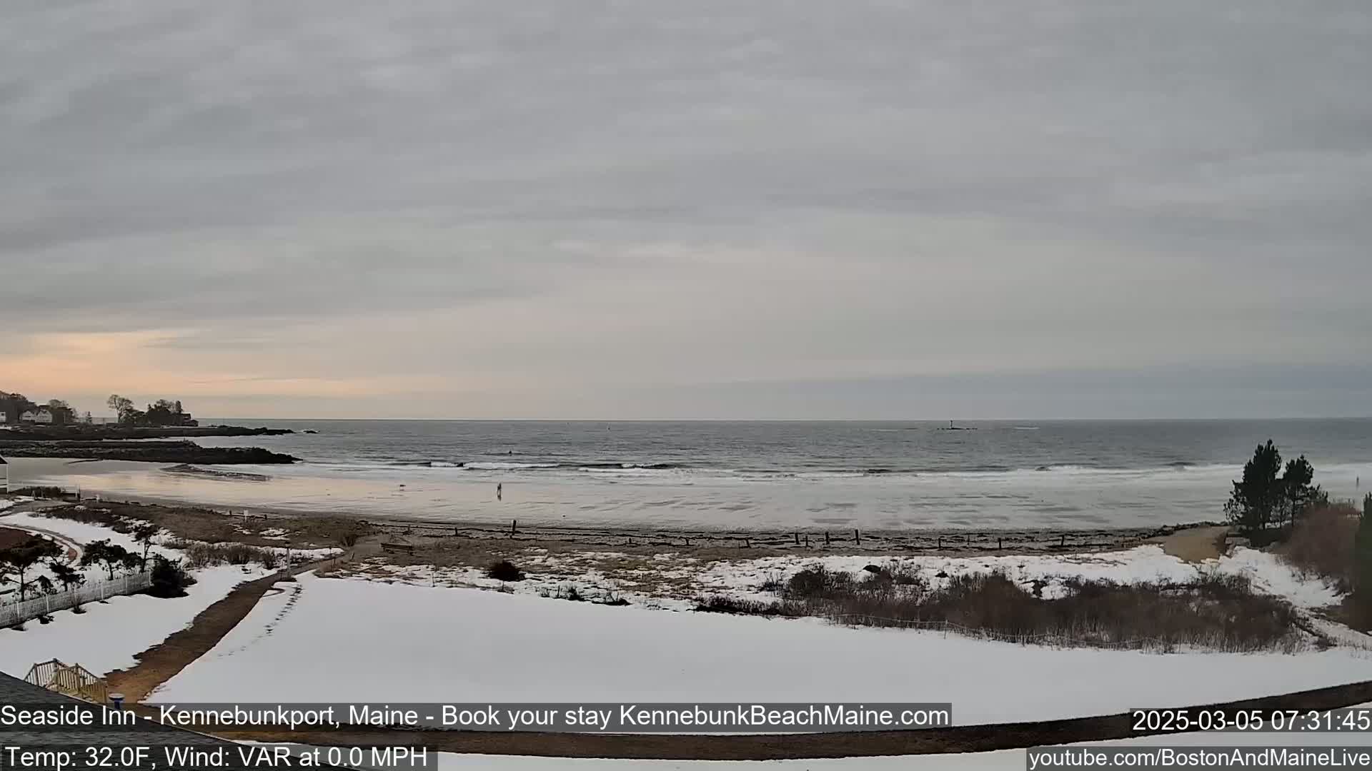A snow-covered beach with a calm ocean under an overcast sky.