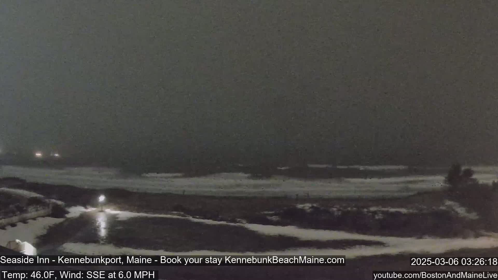 A dark, nighttime scene shows a snow-covered beach with waves crashing on the shore under a heavy, overcast sky.