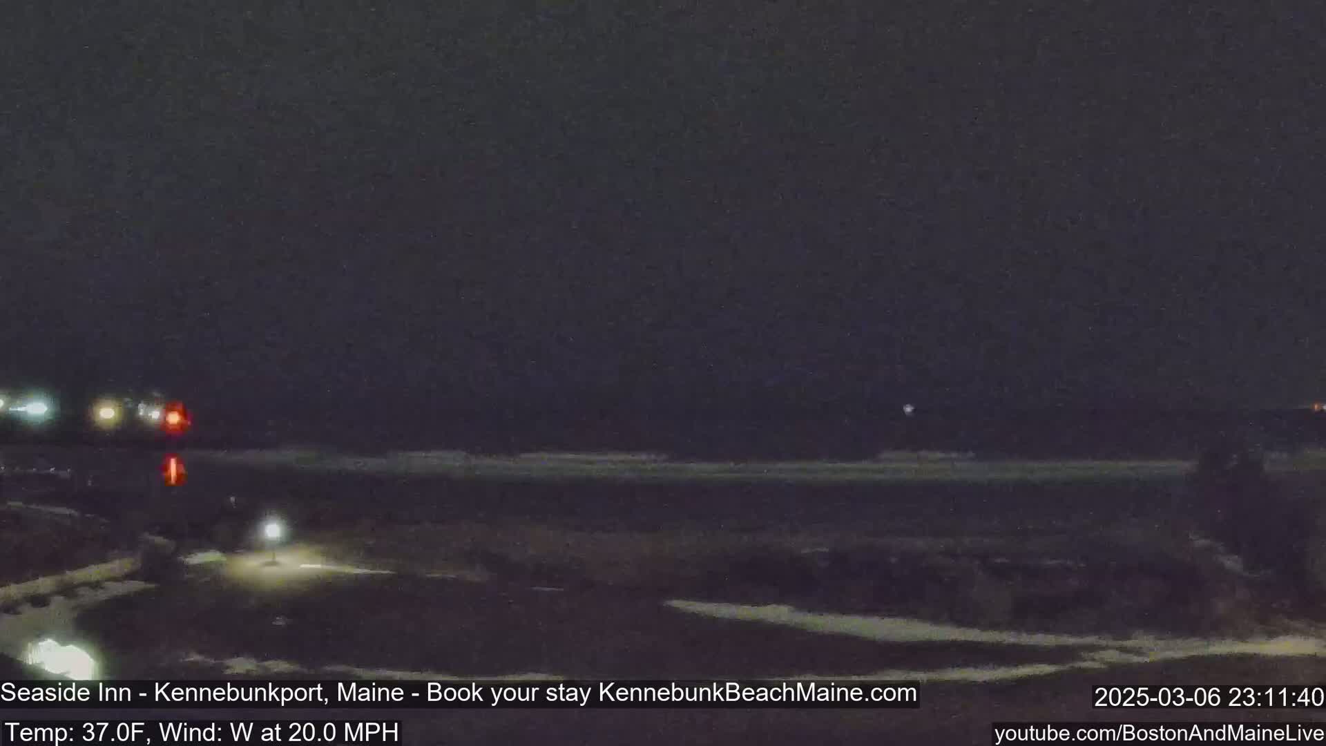 A nighttime, dimly lit coastal road scene shows vehicles driving past a dark beach under a dark sky with a 20 mph westerly wind at 37°F.