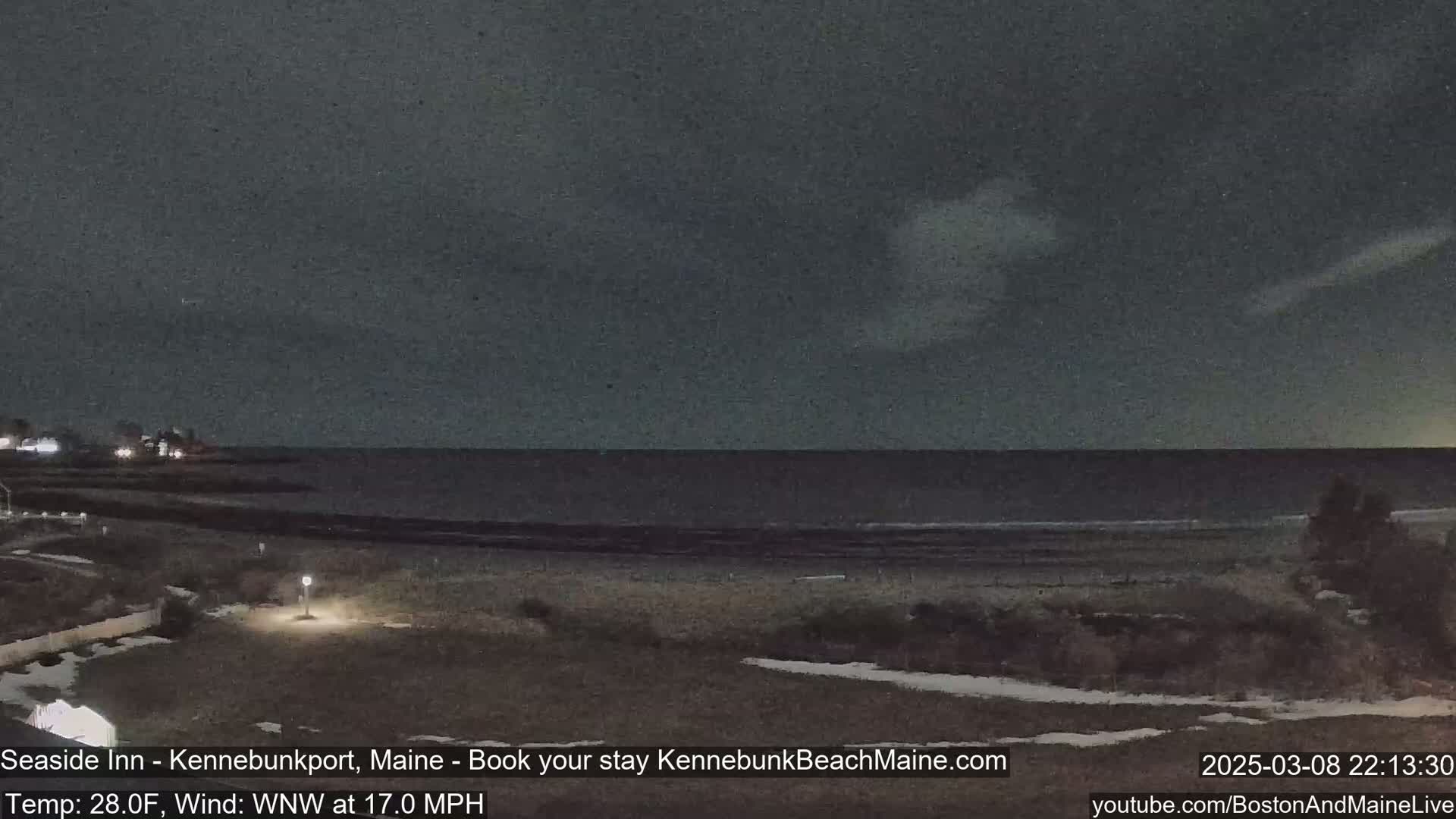 A dark, nighttime view of a beach and ocean under a mostly cloudy sky, with a wind blowing from the west-northwest at 17 mph.