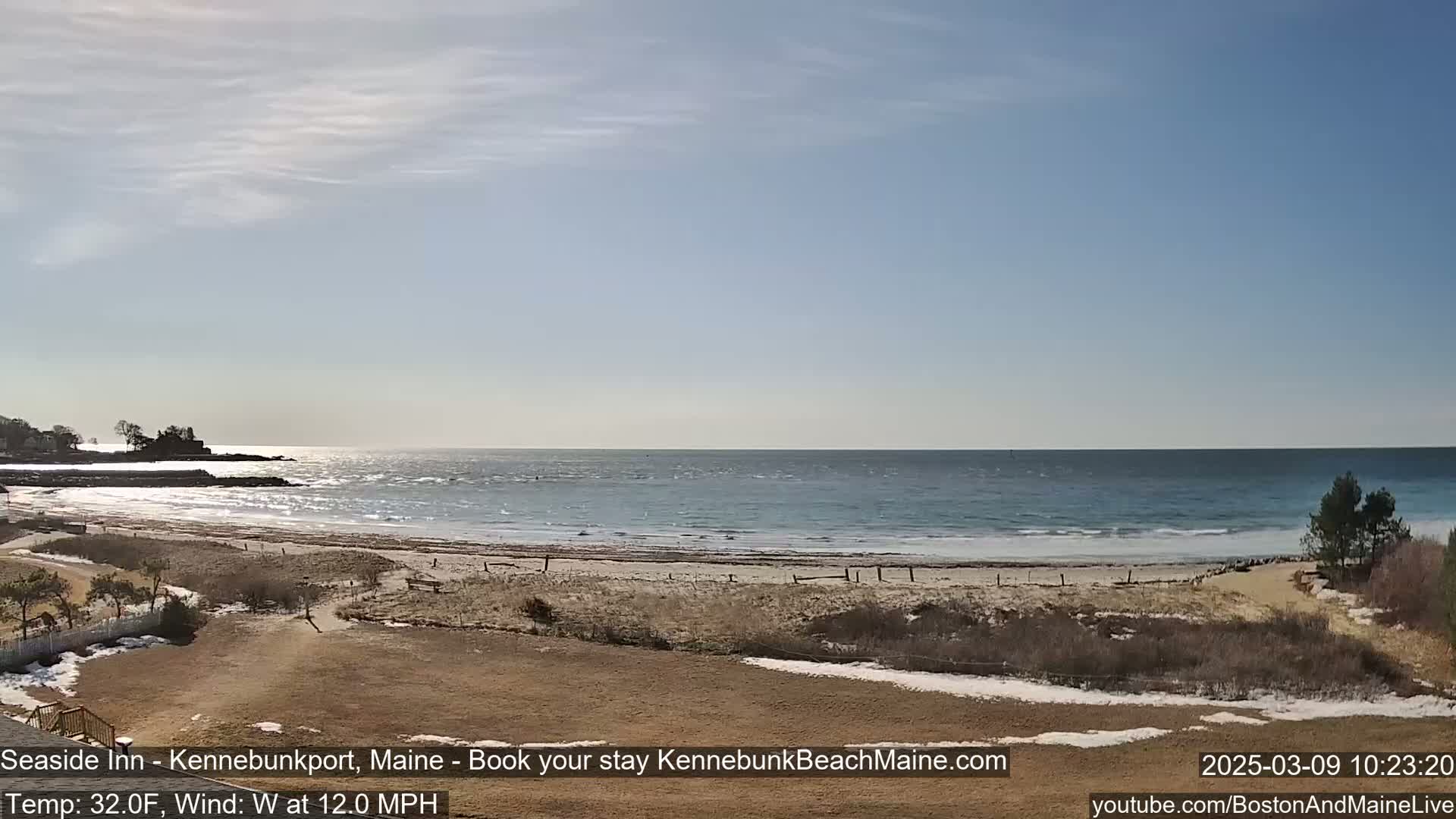 A mostly sunny day with a 12 mph westerly wind shows a sandy beach meeting a somewhat choppy ocean; some patches of snow remain on the land.