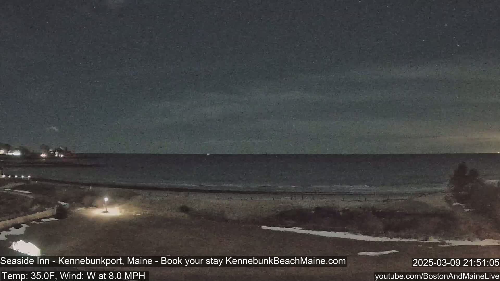 A nighttime view of a dark ocean beach under a mostly clear sky, with a slight wind.