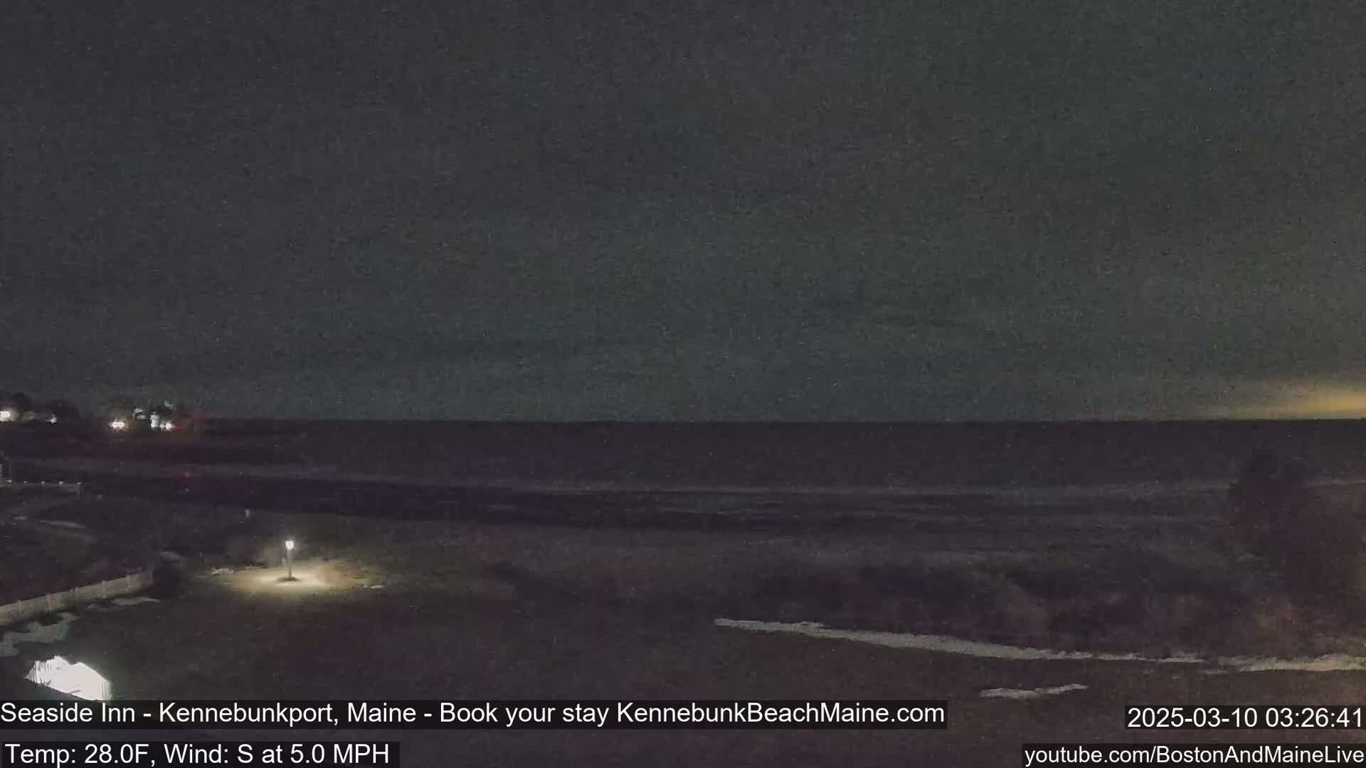 A dark nighttime beach scene shows a calm ocean under a mostly clear sky.