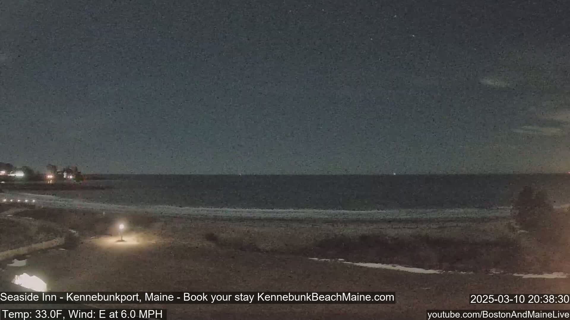 A dark, nighttime beach scene shows a calm ocean under a mostly clear sky with a light east wind and a temperature of 33 degrees Fahrenheit.