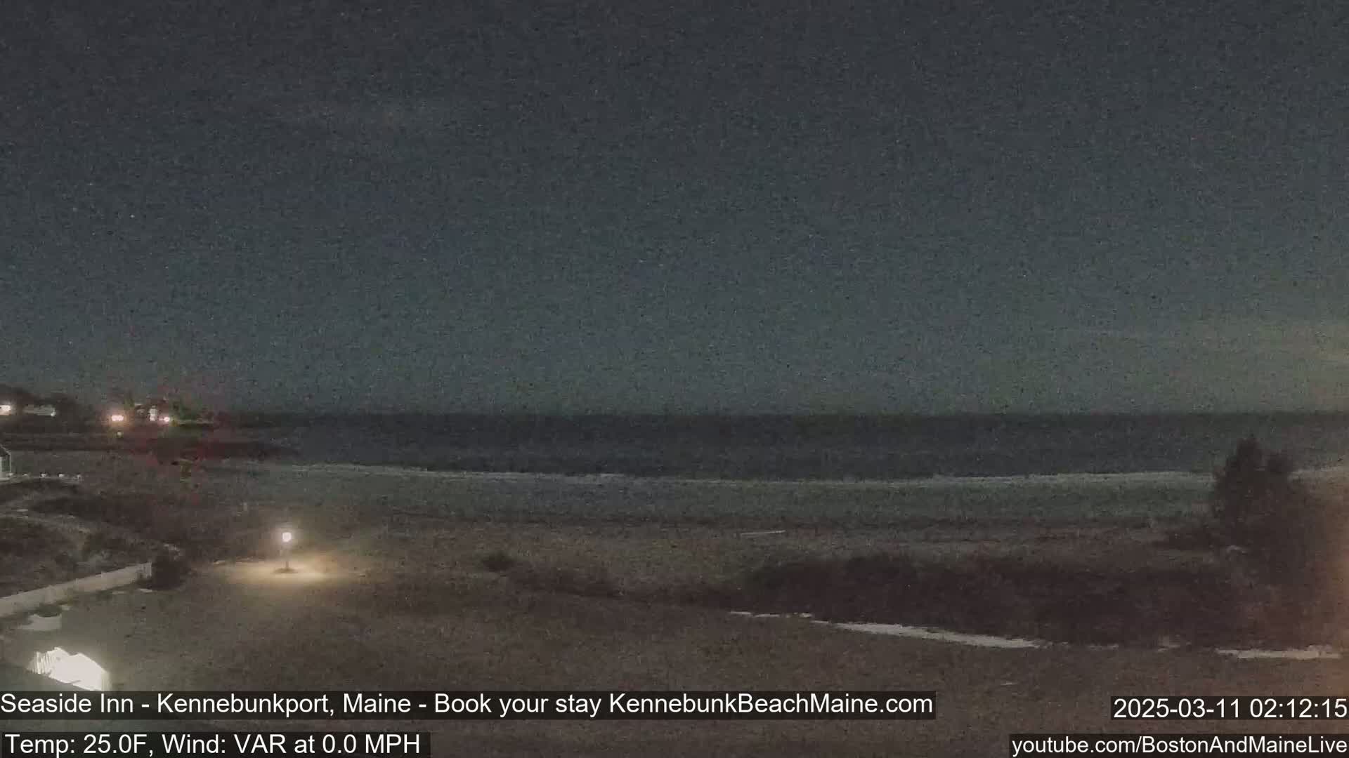 A dark, nighttime beach scene shows a calm ocean under a mostly clear sky; a single lamp illuminates part of the sandy beach.