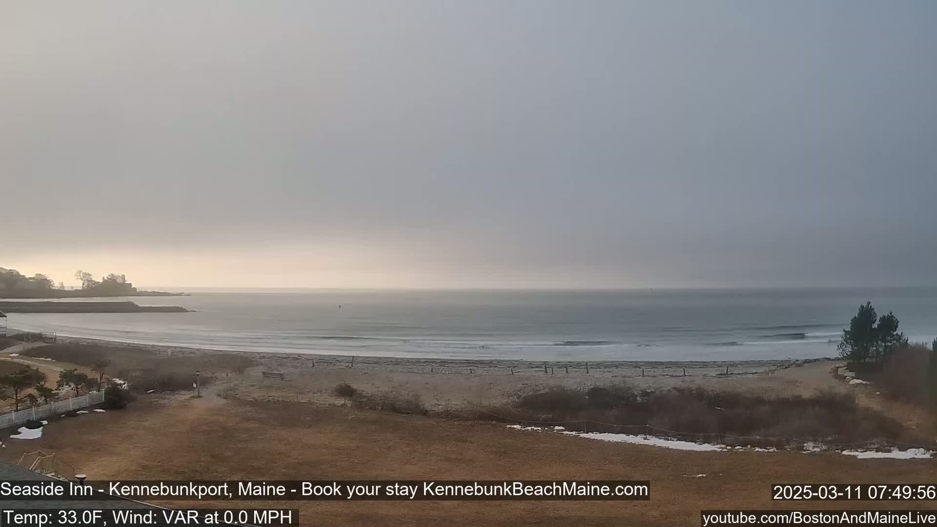 A mostly cloudy, calm day shows a beach with small waves and a calm ocean.