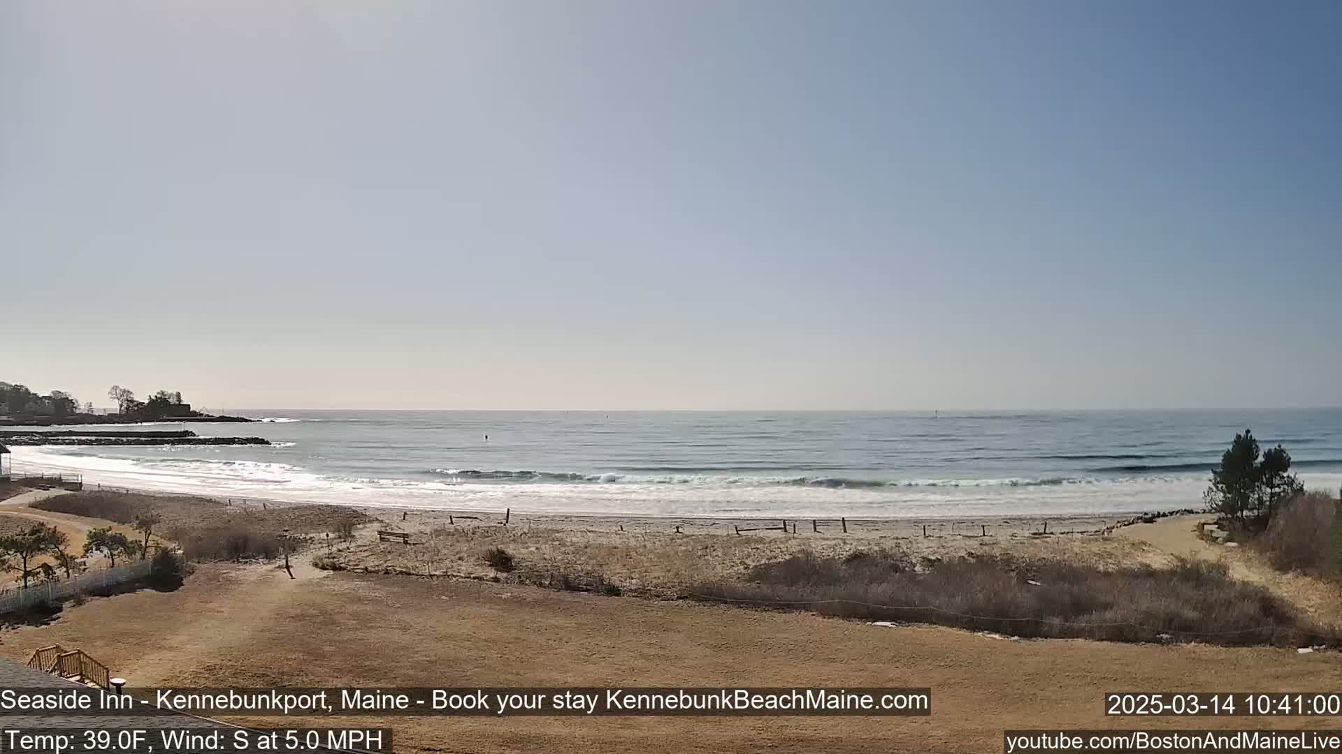 A sandy beach with small waves rolls onto the shore under a clear, bright sky.