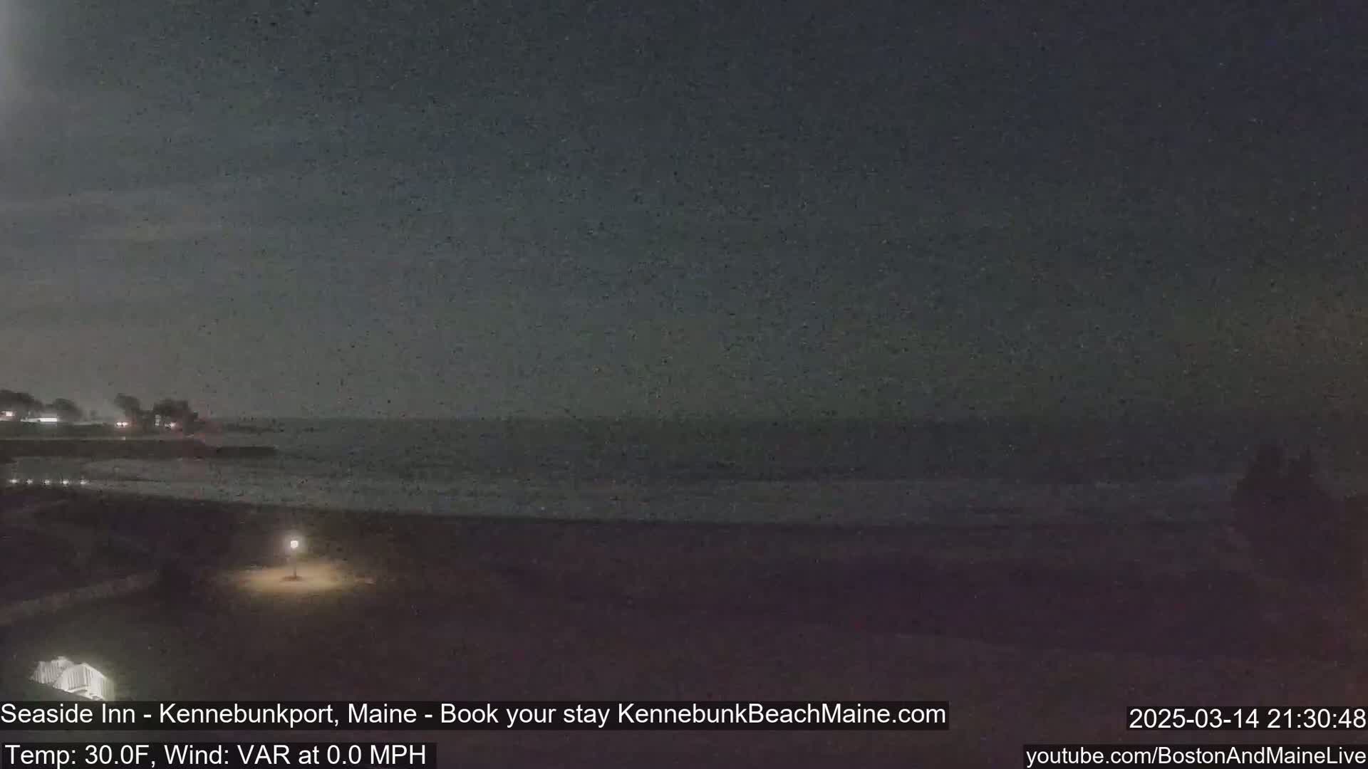 A dark, nighttime beach scene shows a calm ocean under a mostly clear sky.