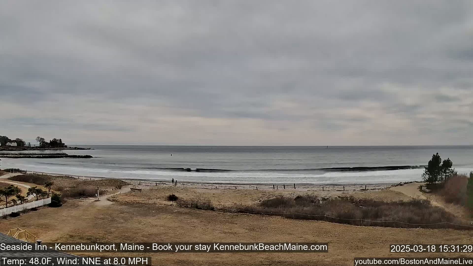 A sandy beach with small waves under an overcast sky.