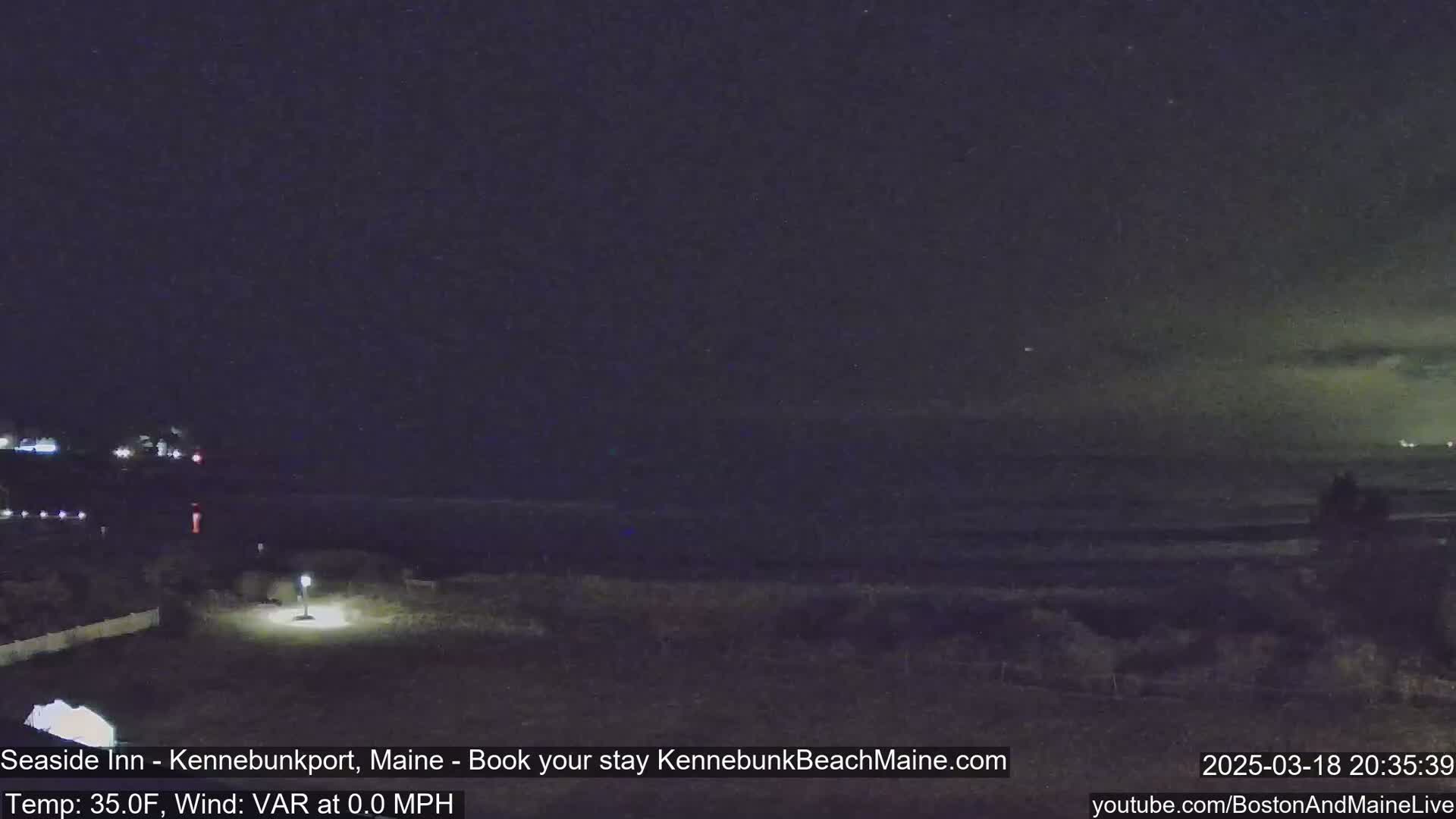A nighttime view of a dark ocean under a mostly clear sky, with a calm beach and a dimly lit foreground.