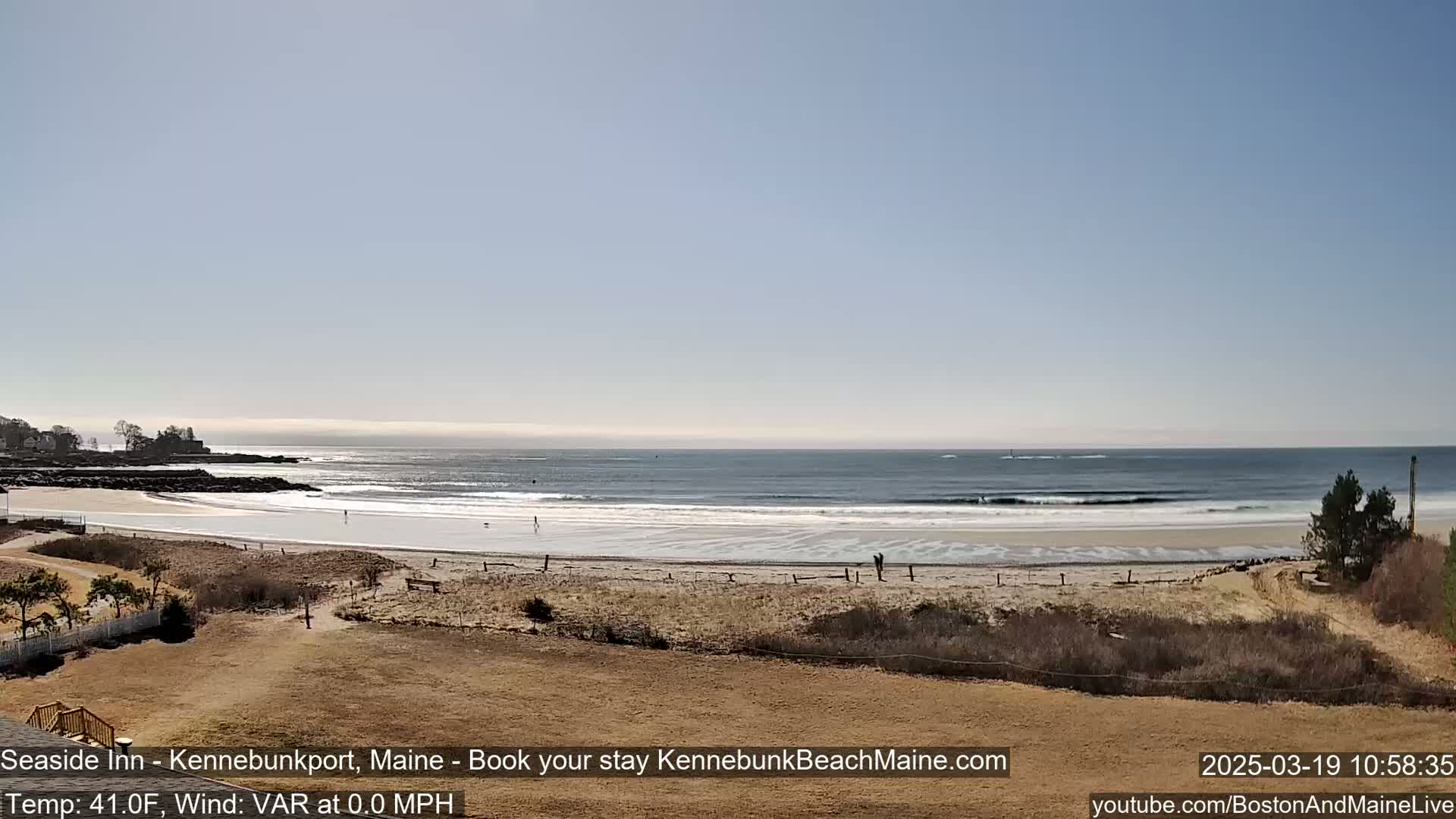 A calm ocean with small waves laps a sandy beach under a clear, bright sky.