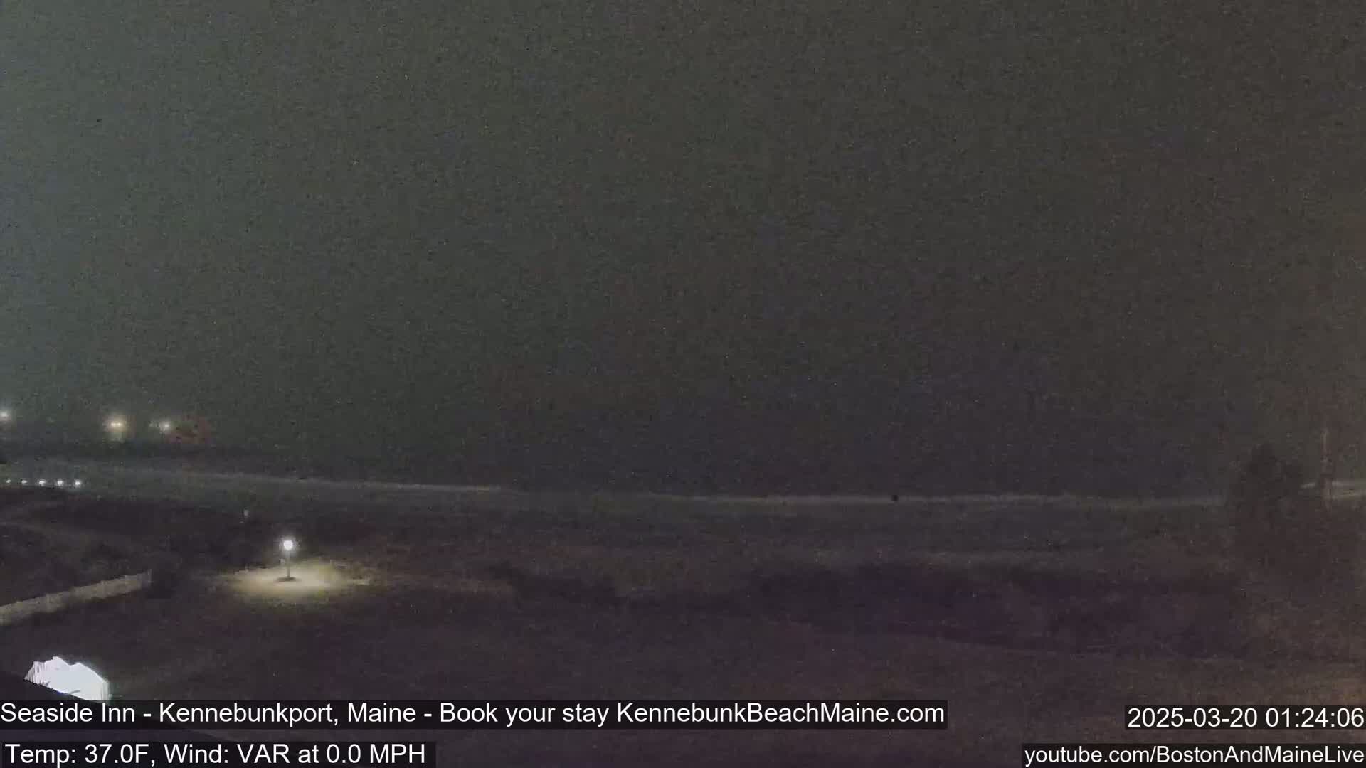 A dark, nighttime beach scene shows a dimly lit shoreline and a dark ocean under an overcast sky.