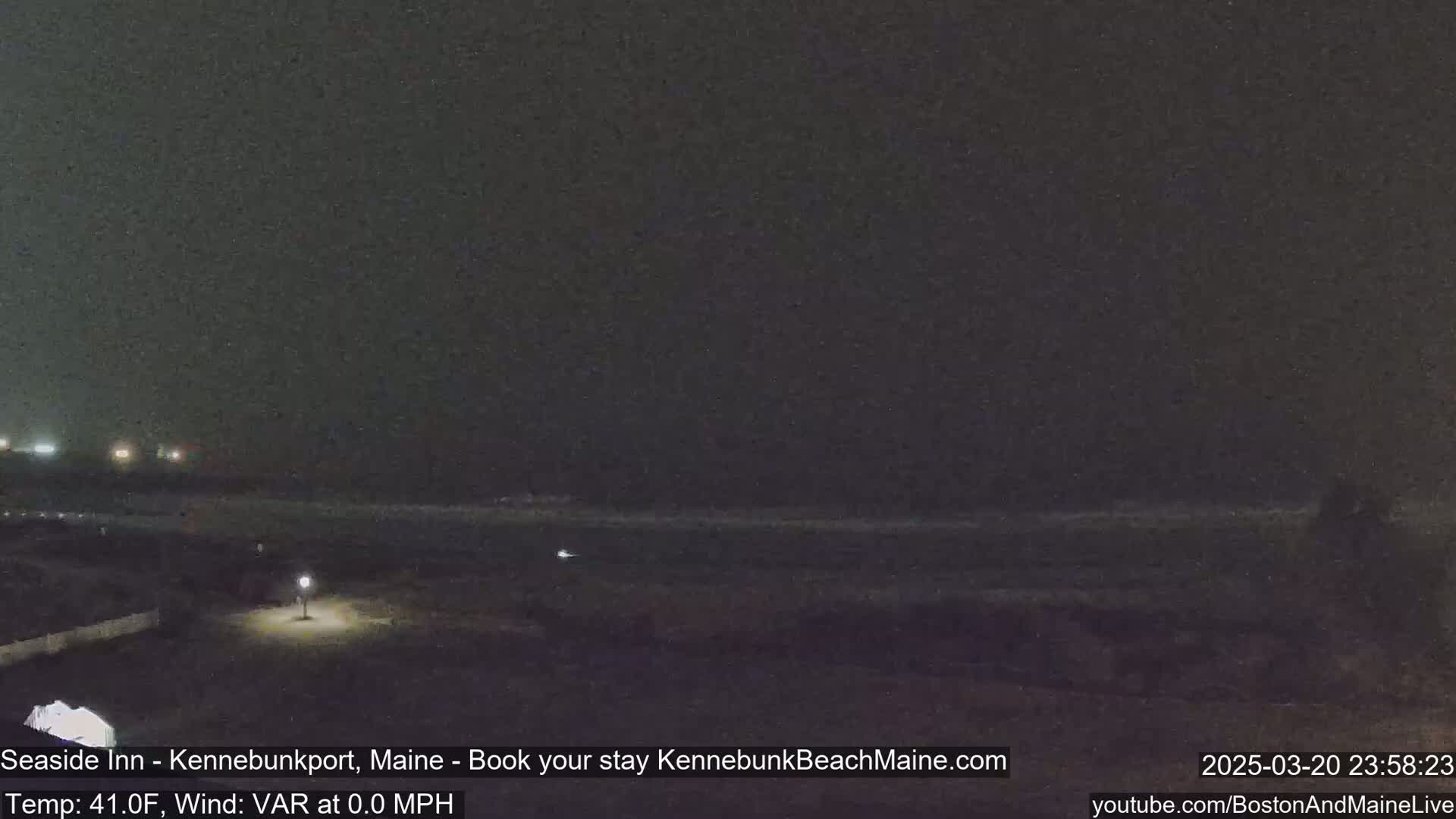 A dark, nighttime beach scene with a calm ocean under an overcast sky.
