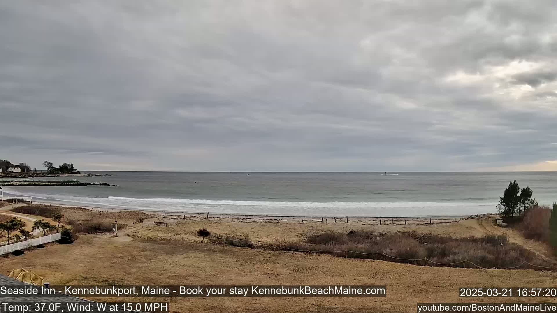 A sandy beach with gentle waves meets a calm ocean under a cloudy sky.