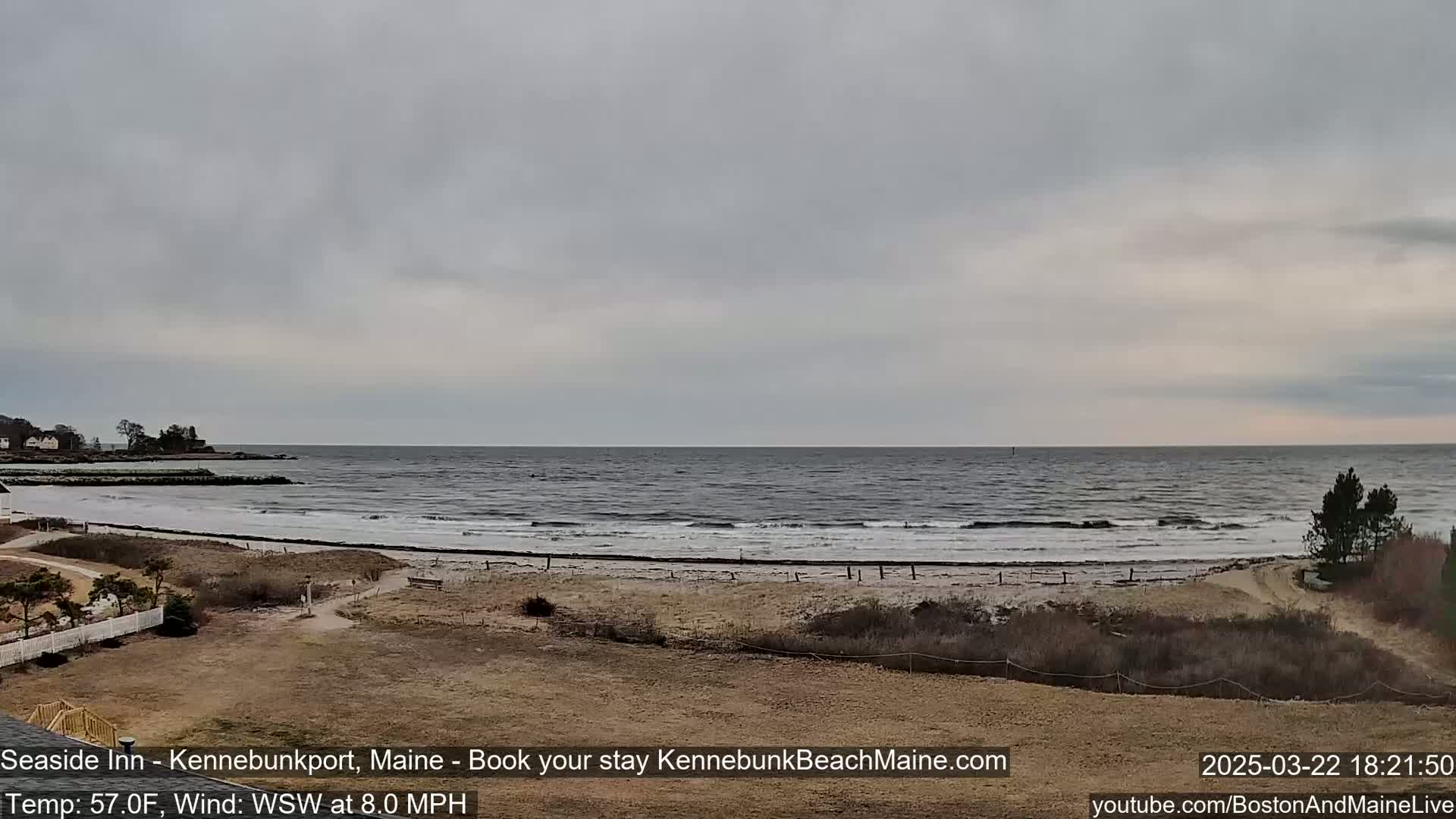 A beach with a calm ocean under an overcast sky is viewed from a slightly elevated vantage point.
