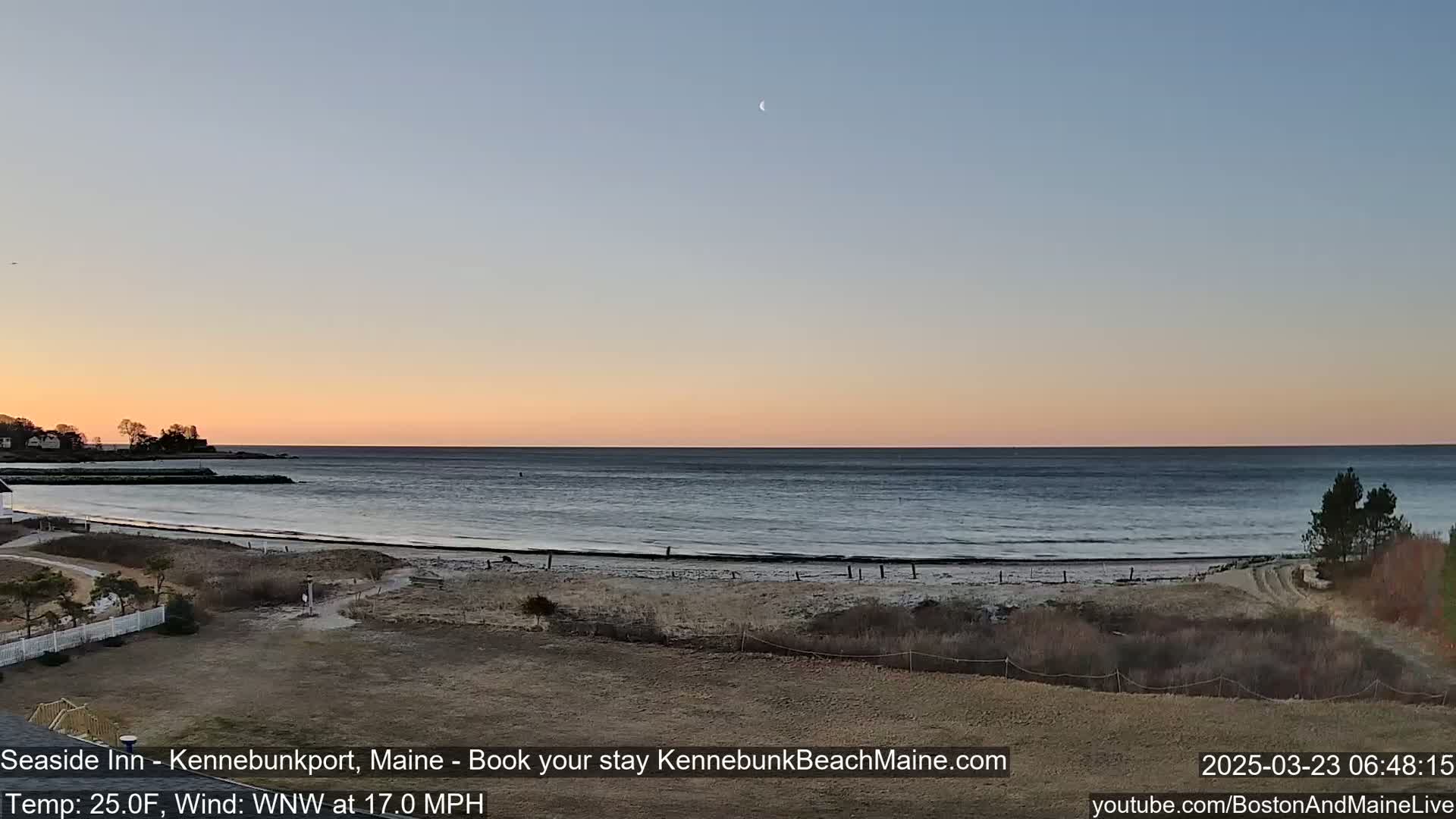 A tranquil beach scene at sunset with a calm ocean, a crescent moon in the sky, and a light wind.