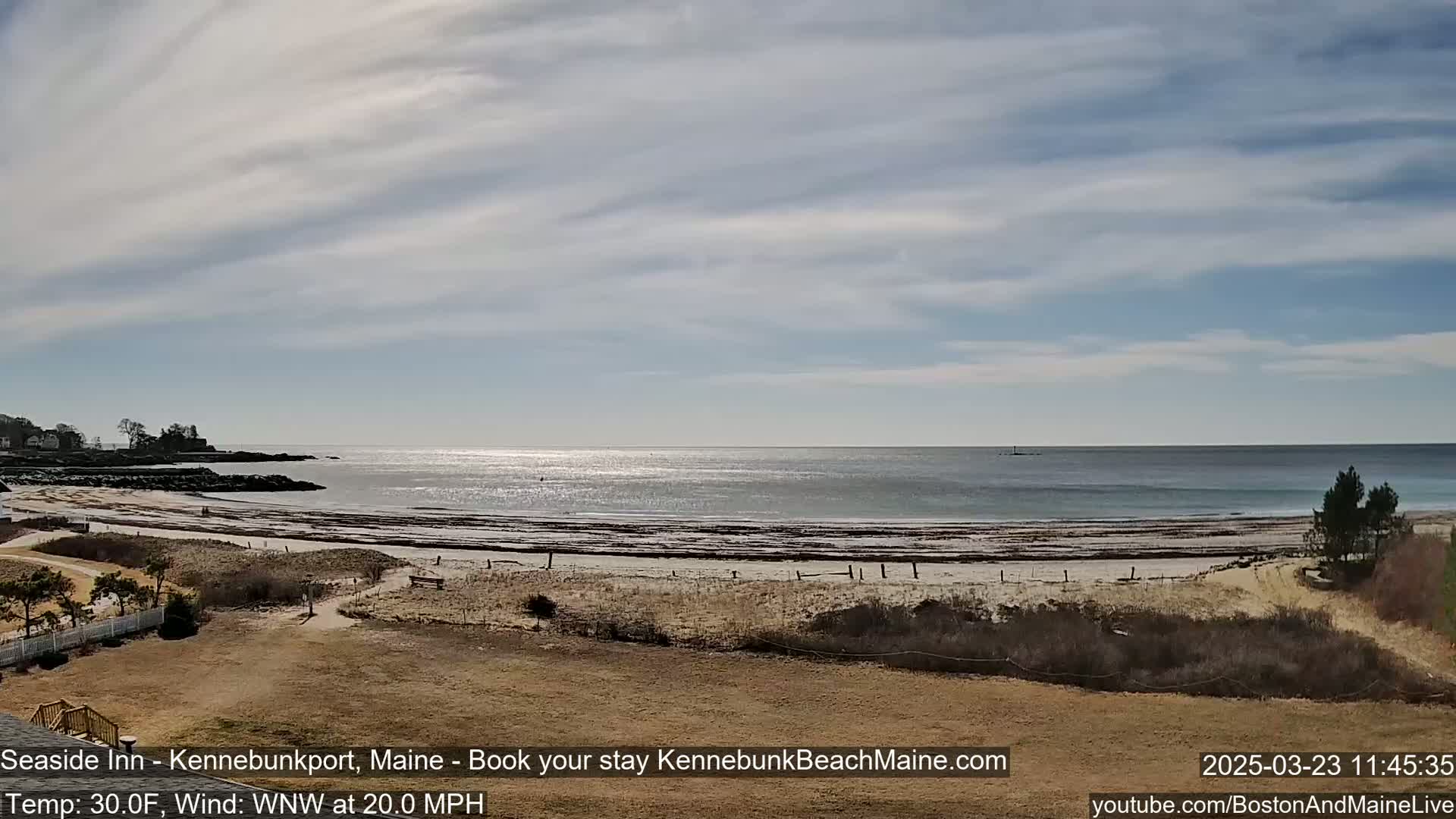 A sandy beach with a calm ocean under a partly cloudy sky.