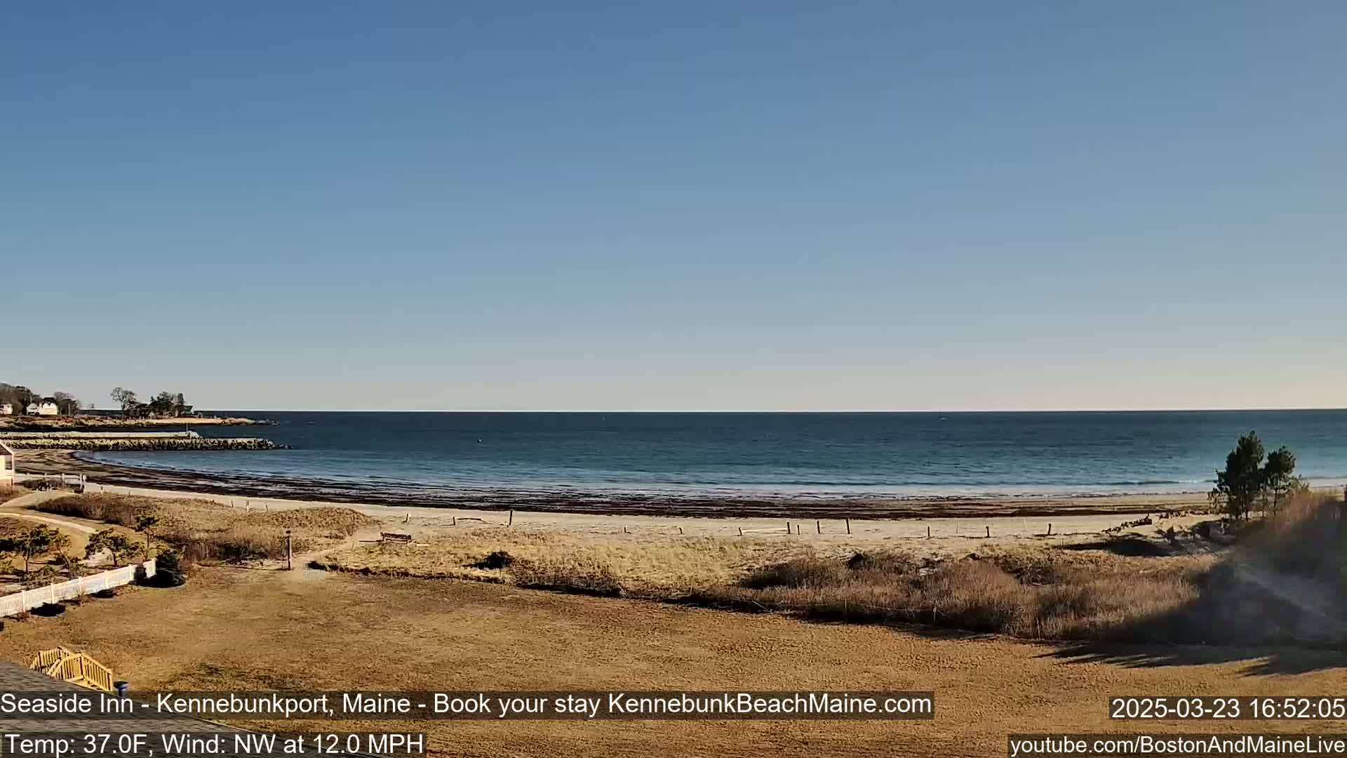 A sandy beach curves along a calm ocean under a clear blue sky.