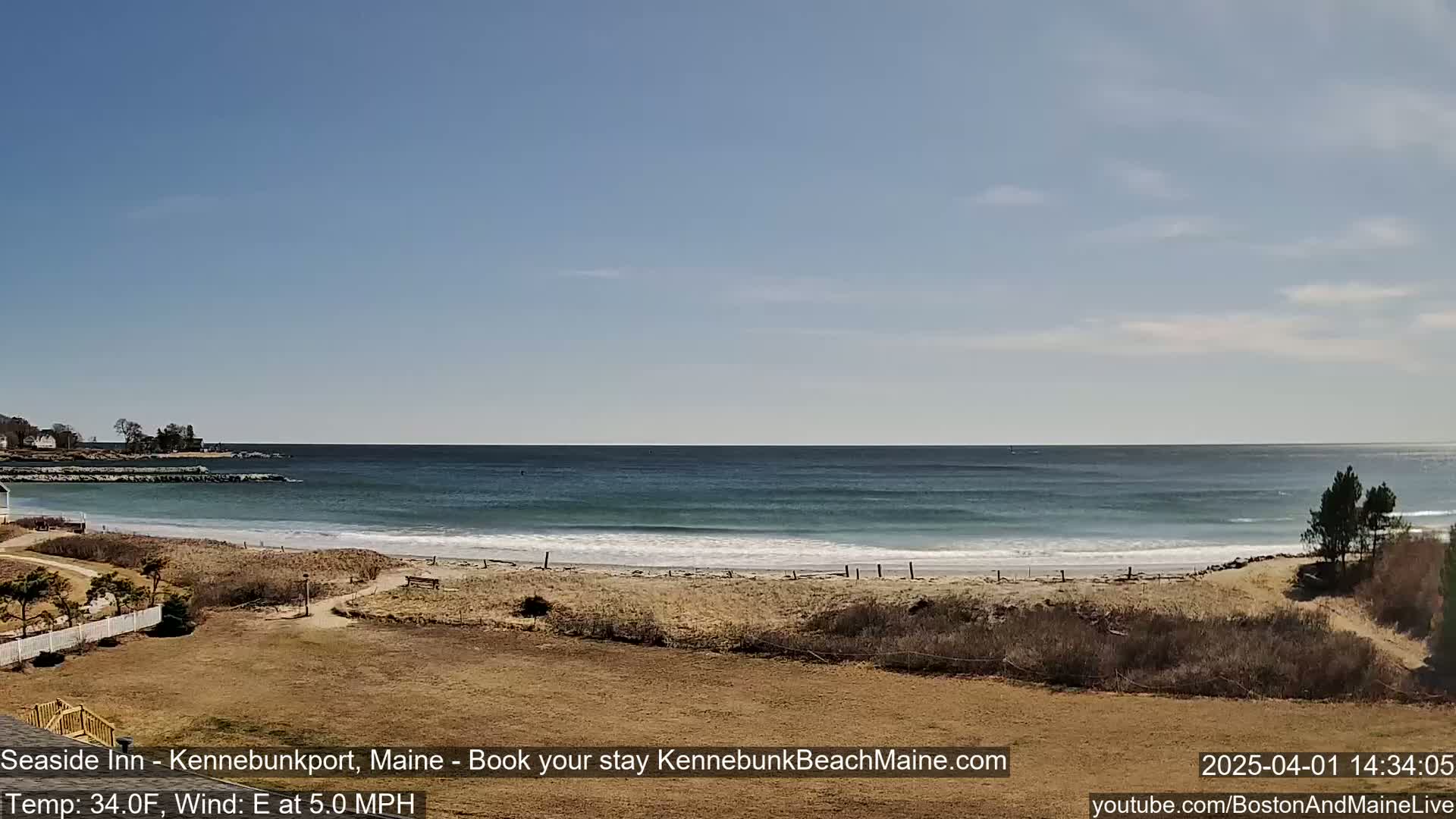 A sandy beach with calm ocean waves under a clear blue sky is visible from a grassy area.