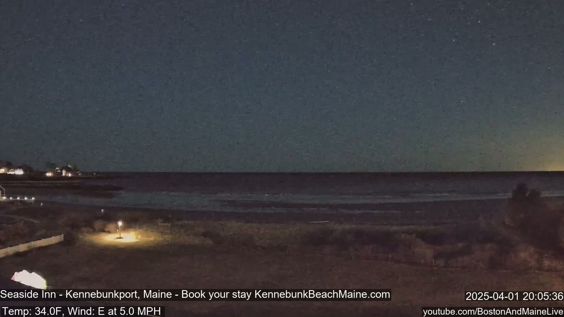 A dark, nighttime beach scene shows a calm ocean under a clear, starry sky with a slight easterly wind.