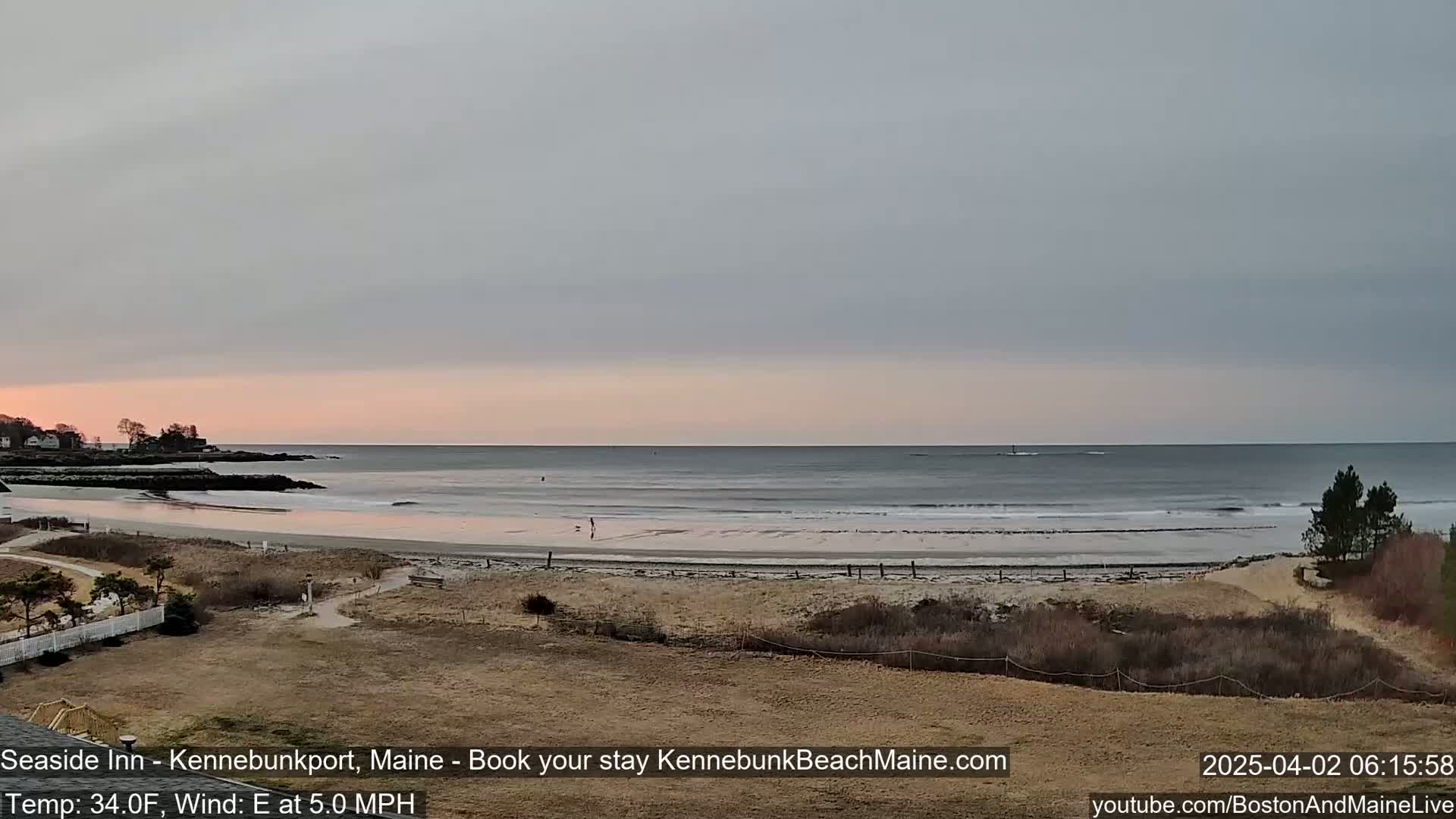 A sandy beach with calm waves under an overcast sky at sunrise.