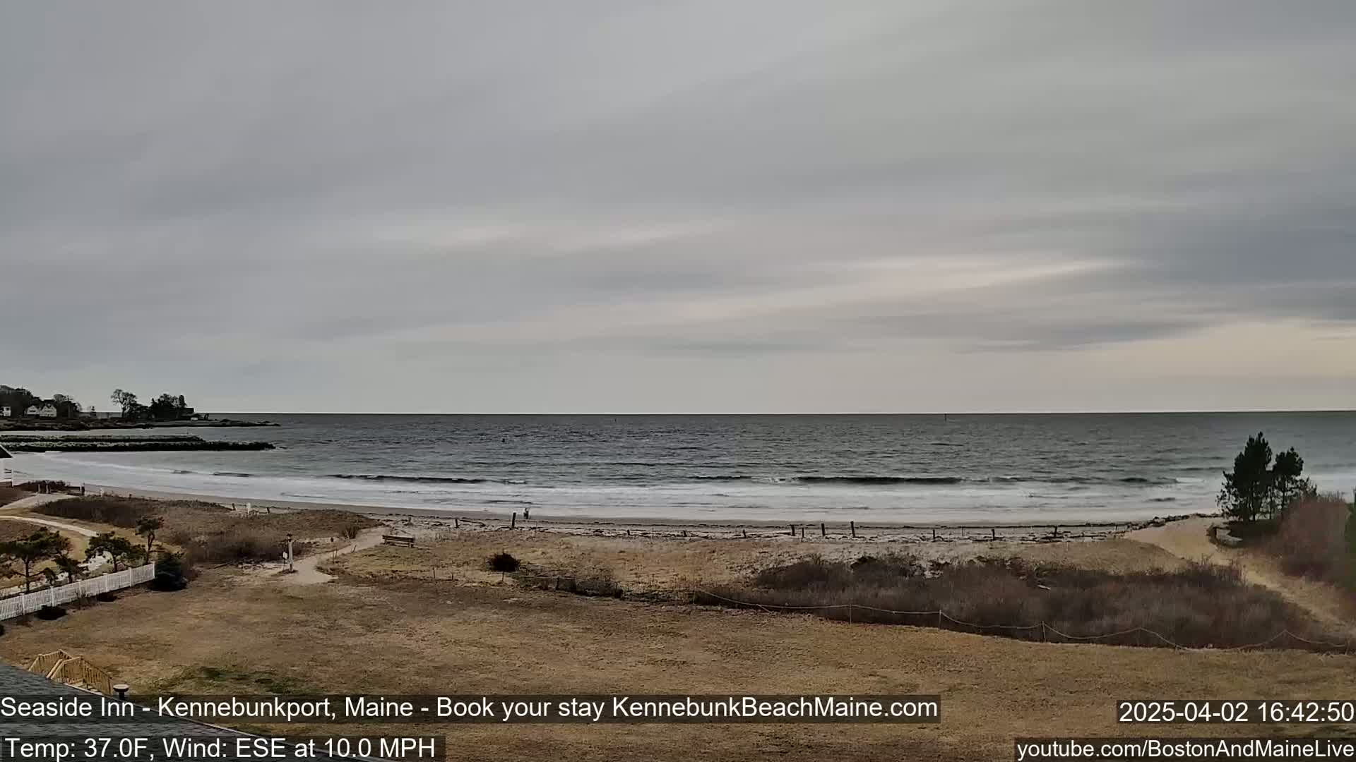 A wide, sandy beach with gentle waves rolls onto the shore under an overcast sky.