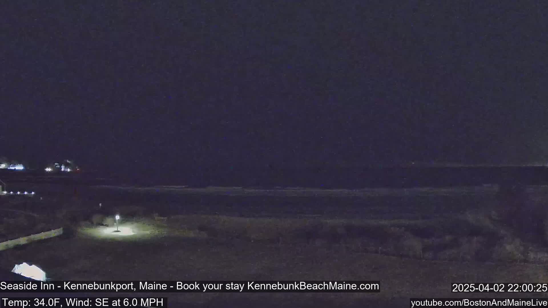 A nighttime view of a dark ocean under a clear, dark sky, with a dimly lit shoreline in the foreground.