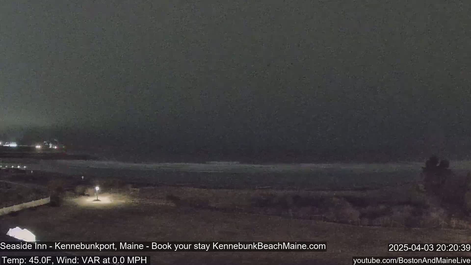 A dark, nighttime view of a calm ocean shore under a cloudy sky.