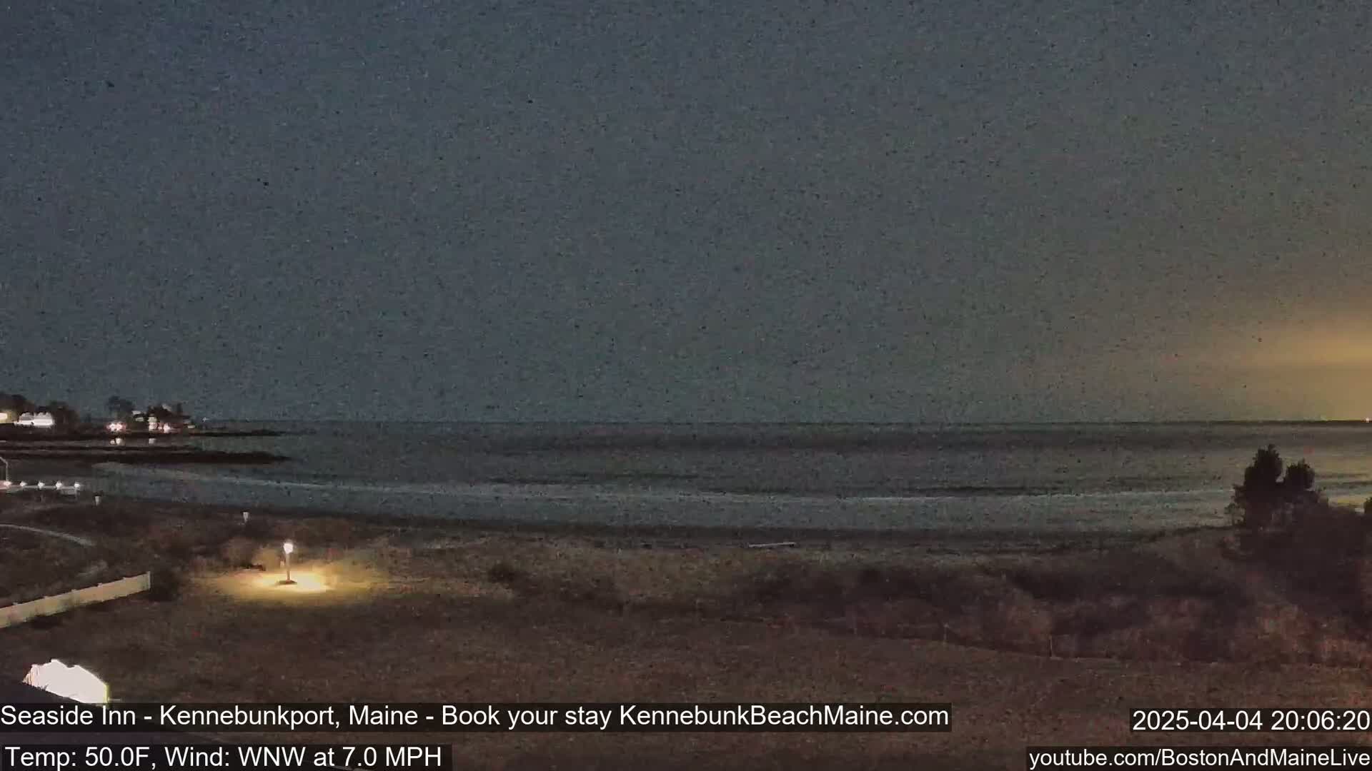 A dark, nighttime beach scene shows a calm ocean under a dusky sky with a gentle wind.