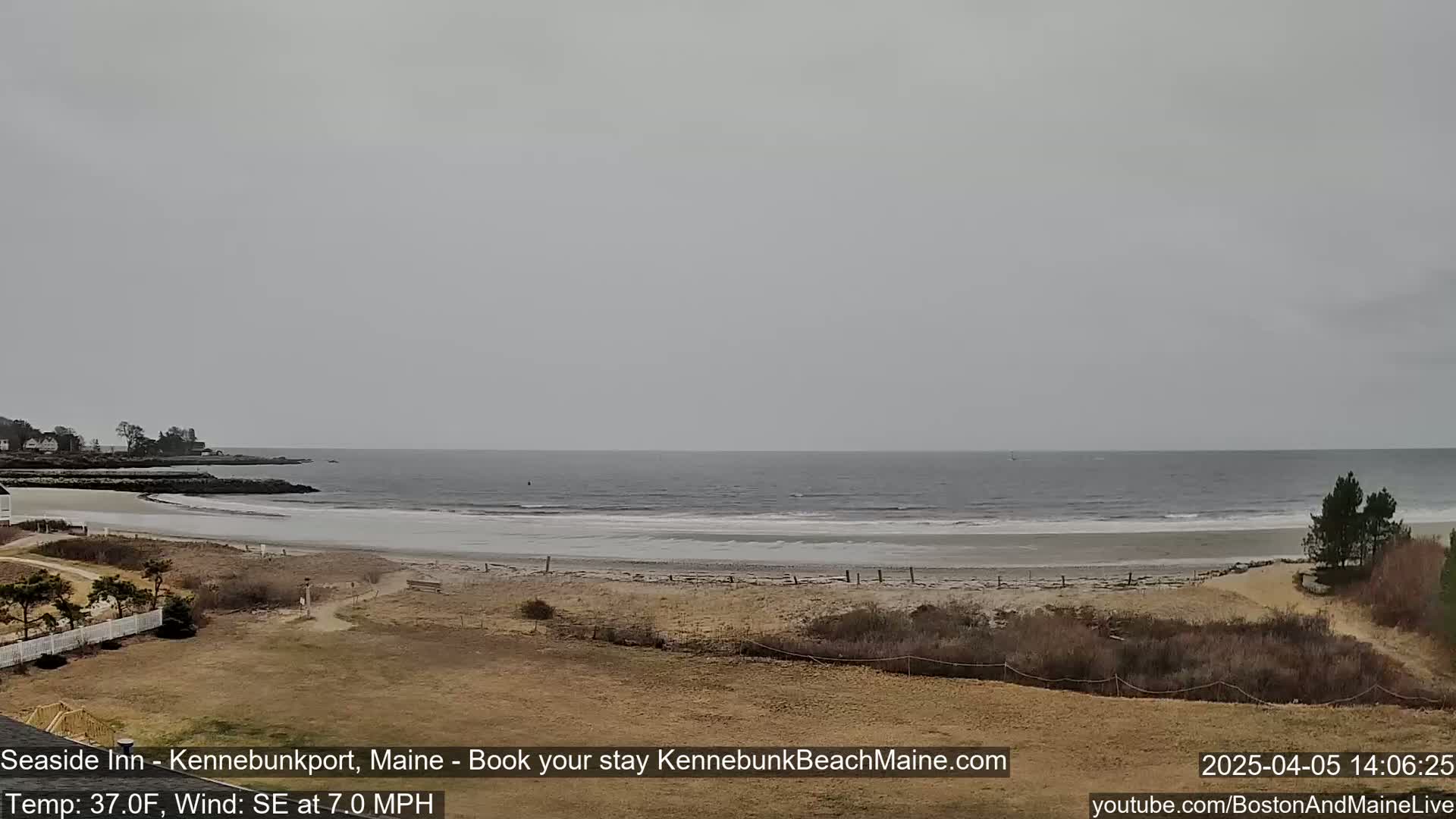 A wide, sandy beach stretches to a calm, gray ocean under an overcast sky.