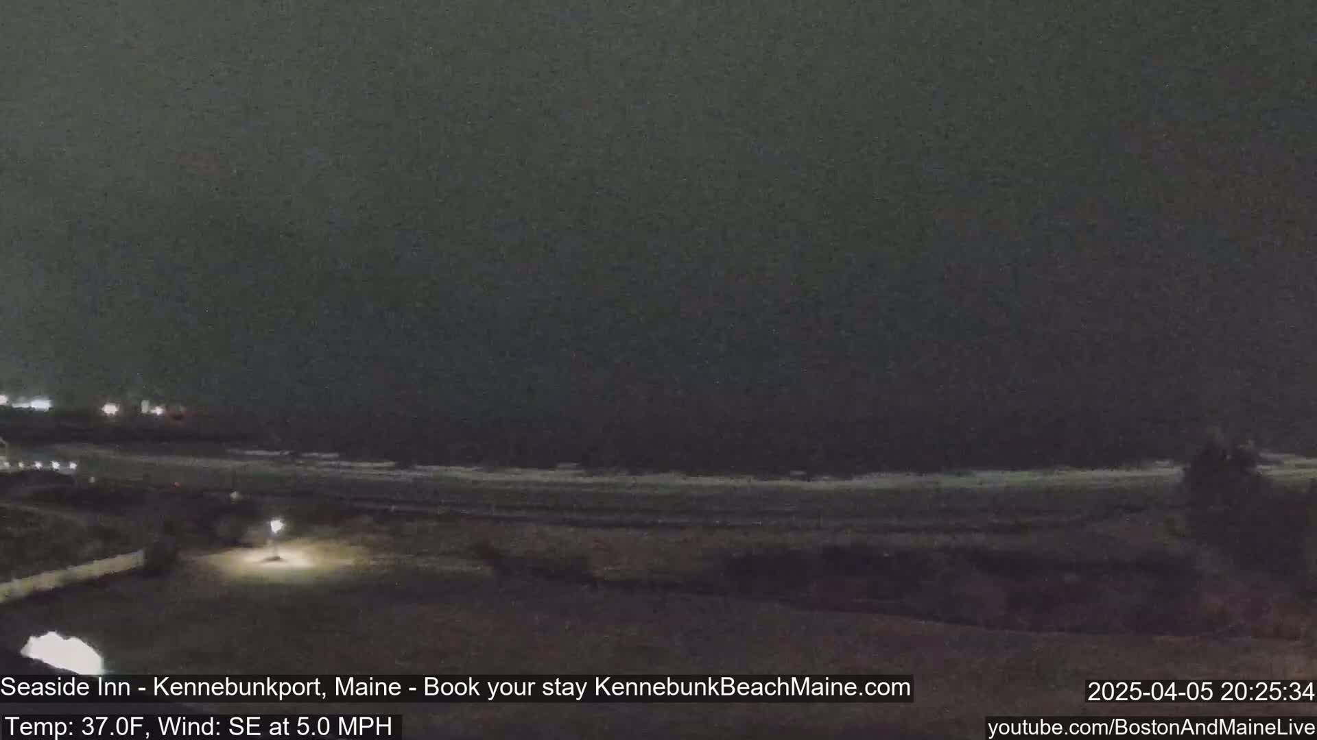 A dark, nighttime beach scene shows a dimly lit shoreline and ocean with small waves under a dark, overcast sky.