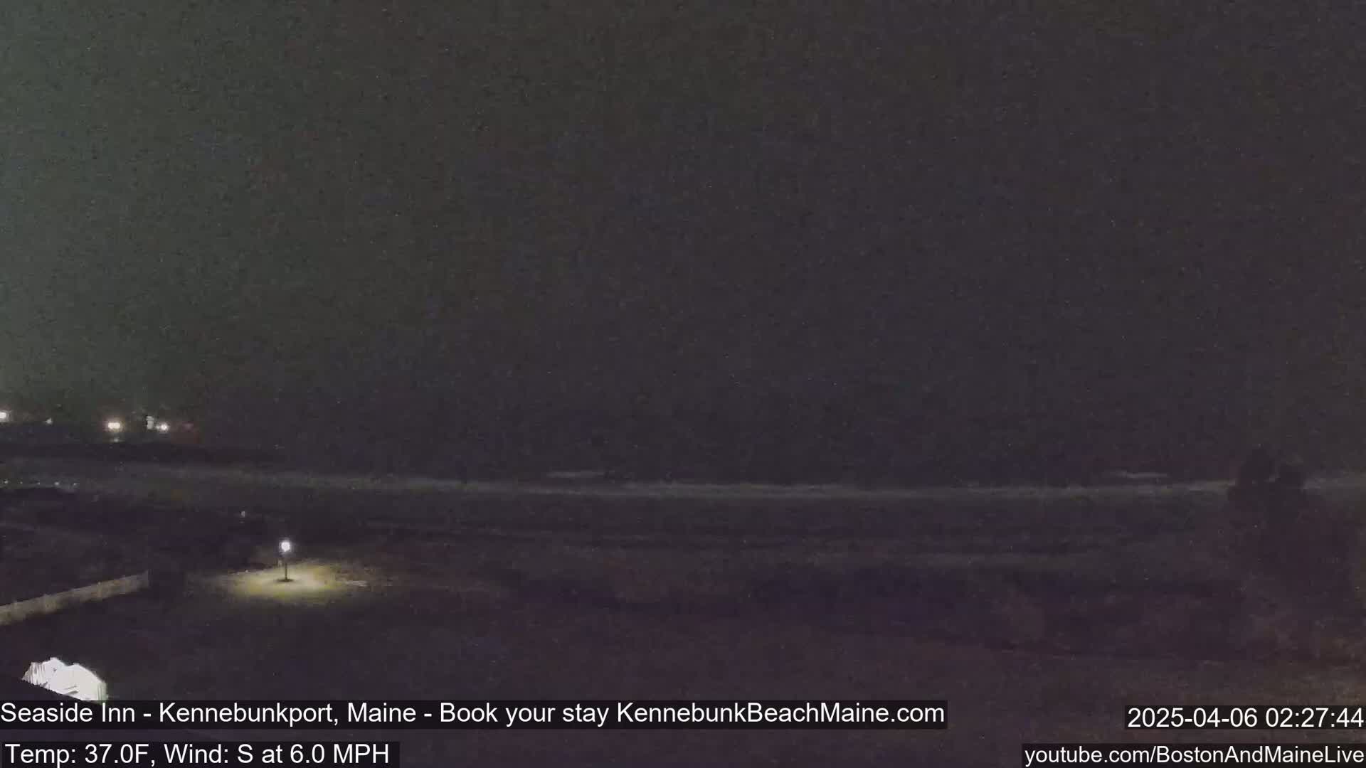 A nighttime, dark beach scene with a calm ocean under a cloudy sky.