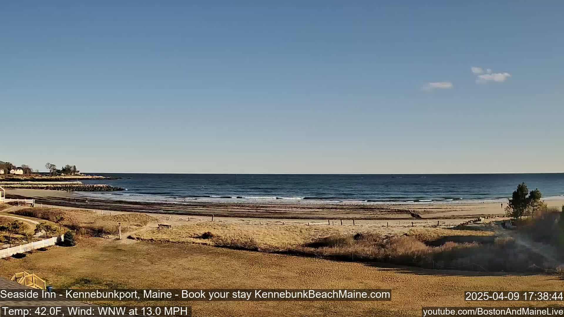 A sandy beach with a calm ocean and a clear blue sky is visible from a vantage point on a grassy hill.