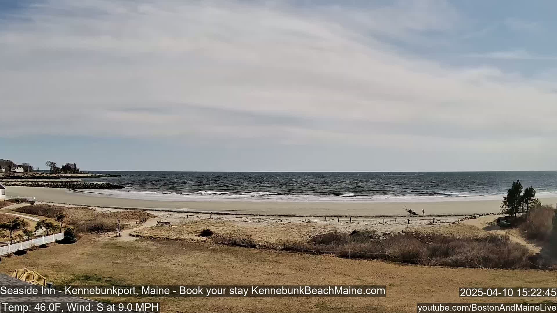 A sandy beach stretches along a calm ocean under a partly cloudy sky.
