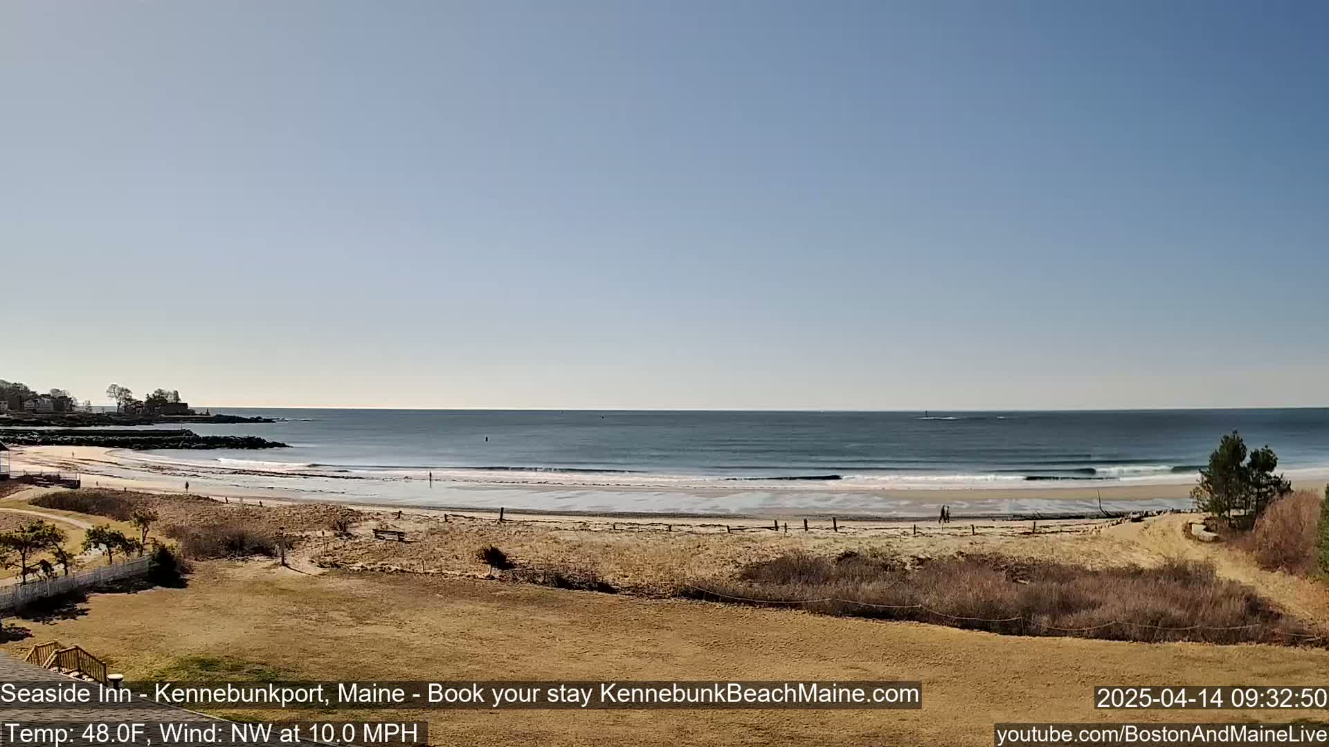 A sandy beach stretches along a calm ocean under a clear, bright sky.