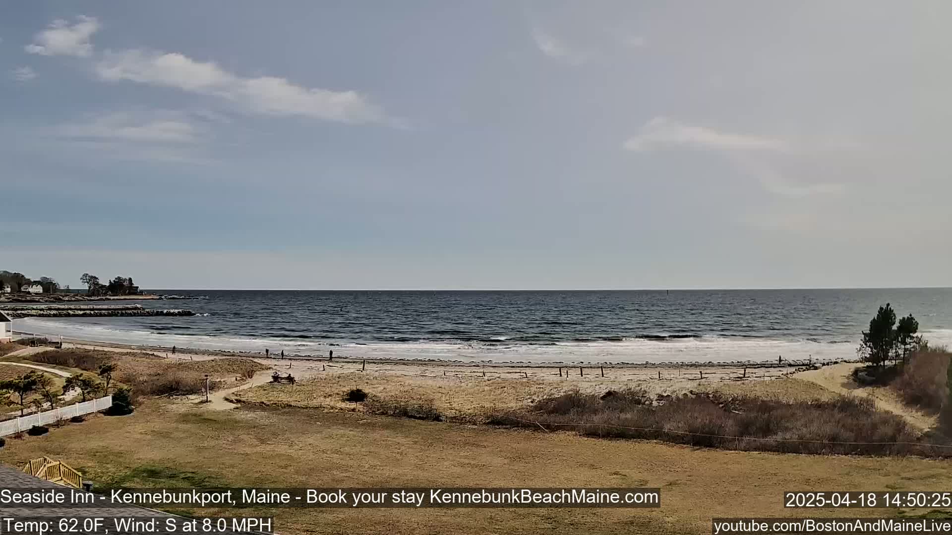 A sandy beach stretches along a calm ocean under a mostly clear sky.