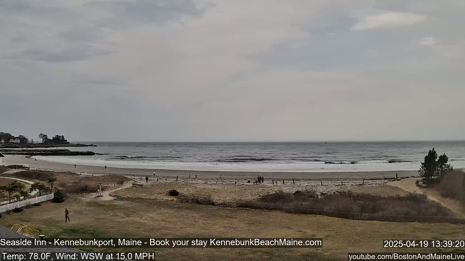 A sandy beach with a few people on it stretches along a gray, somewhat overcast ocean under a cloudy sky.